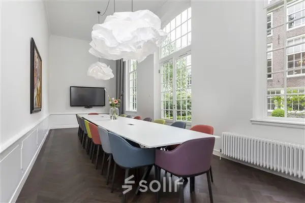 Bright, modern office space rental in Amsterdam Canal Belt, featuring a long table with colorful chairs under unique pendant lights, perfect for meetings.