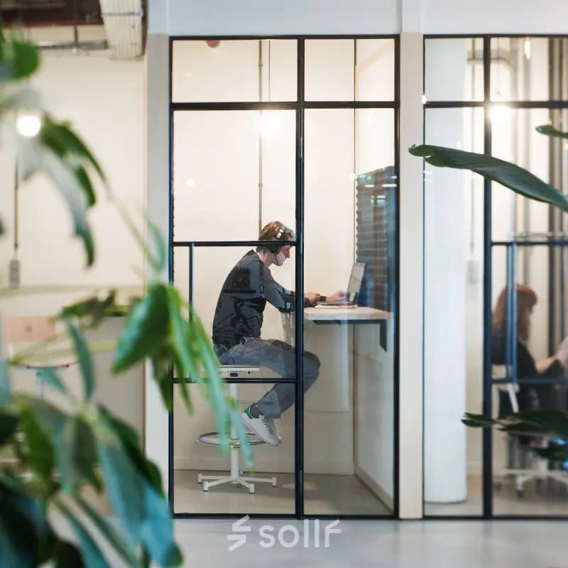 Two people working in a modern, glass-enclosed office space for rent on Singel 542, Amsterdam Canal Belt.