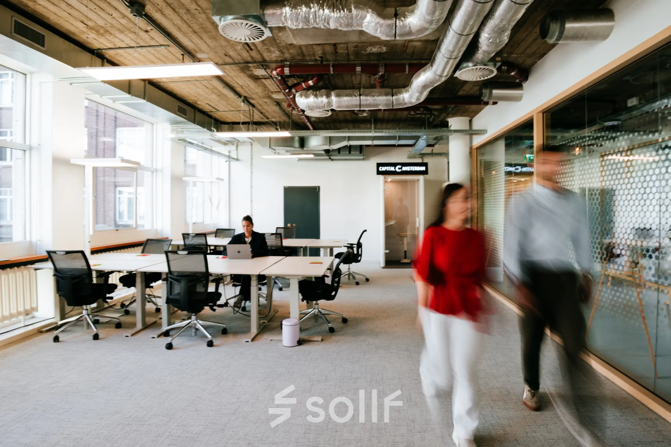 Modern office space at Singel 542, Amsterdam Canal Belt, with people working at desks and others walking. Perfect for office space rental.