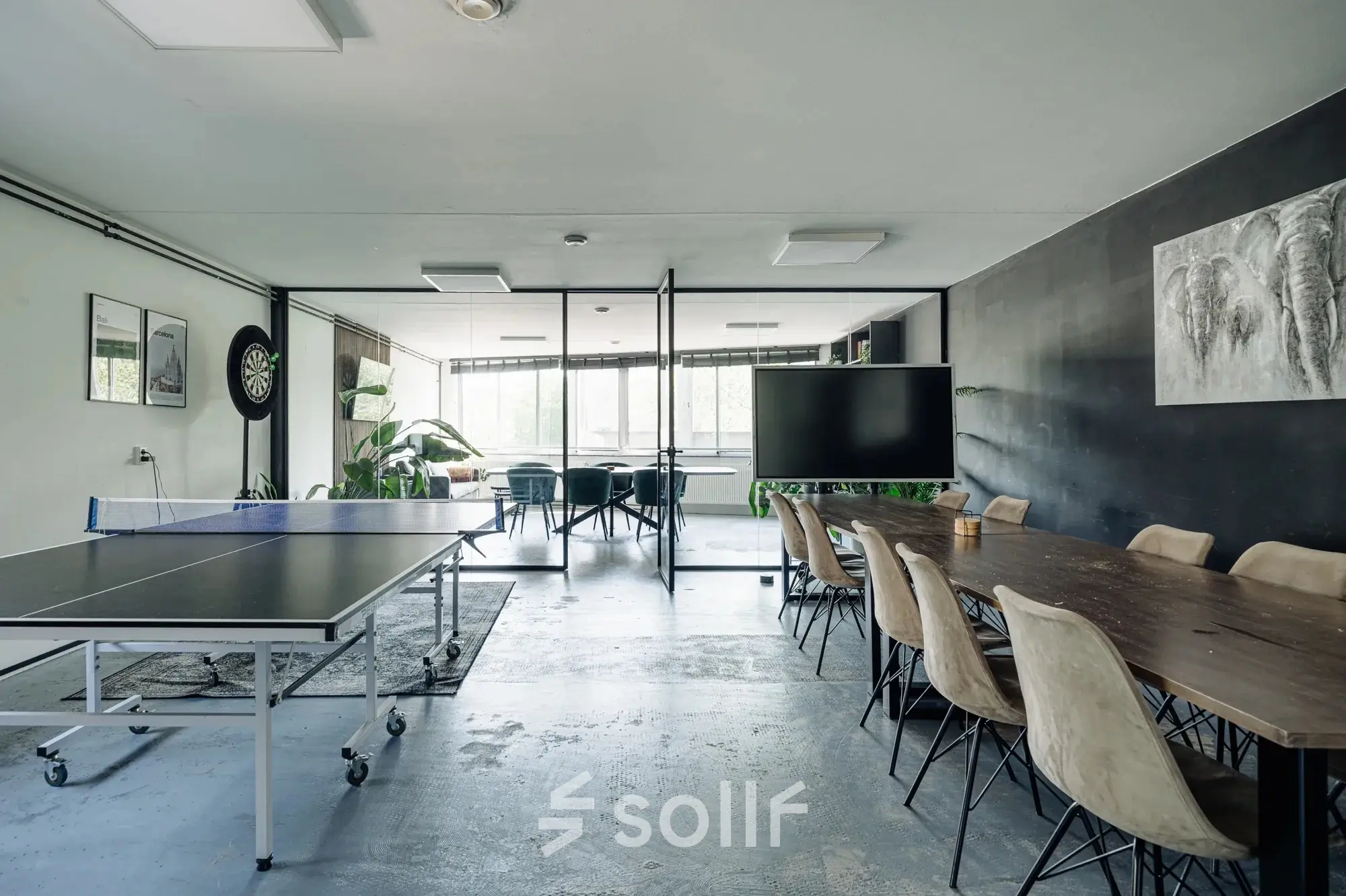 A spacious office at Weesperstraat 394-396 with a meeting table, wall art, dartboard, and ping pong table, ideal for office space rental in Amsterdam Canal Belt.