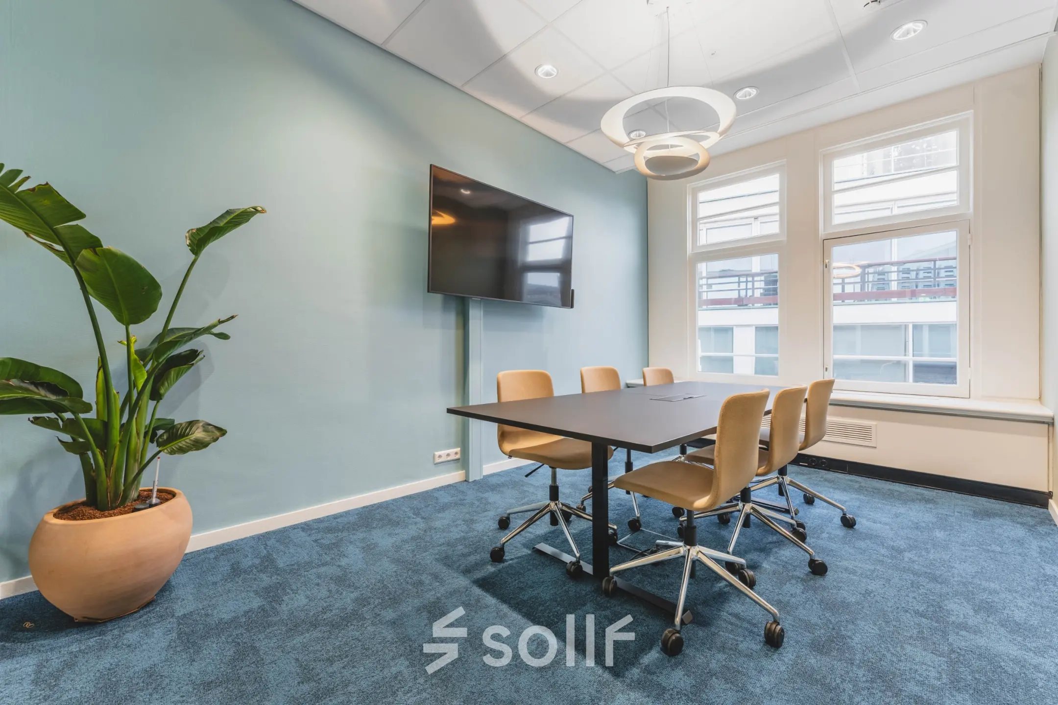 Bright office space with a meeting table, chairs, and a wall-mounted TV at Herengracht 471, perfect for office space rental in Amsterdam Center.