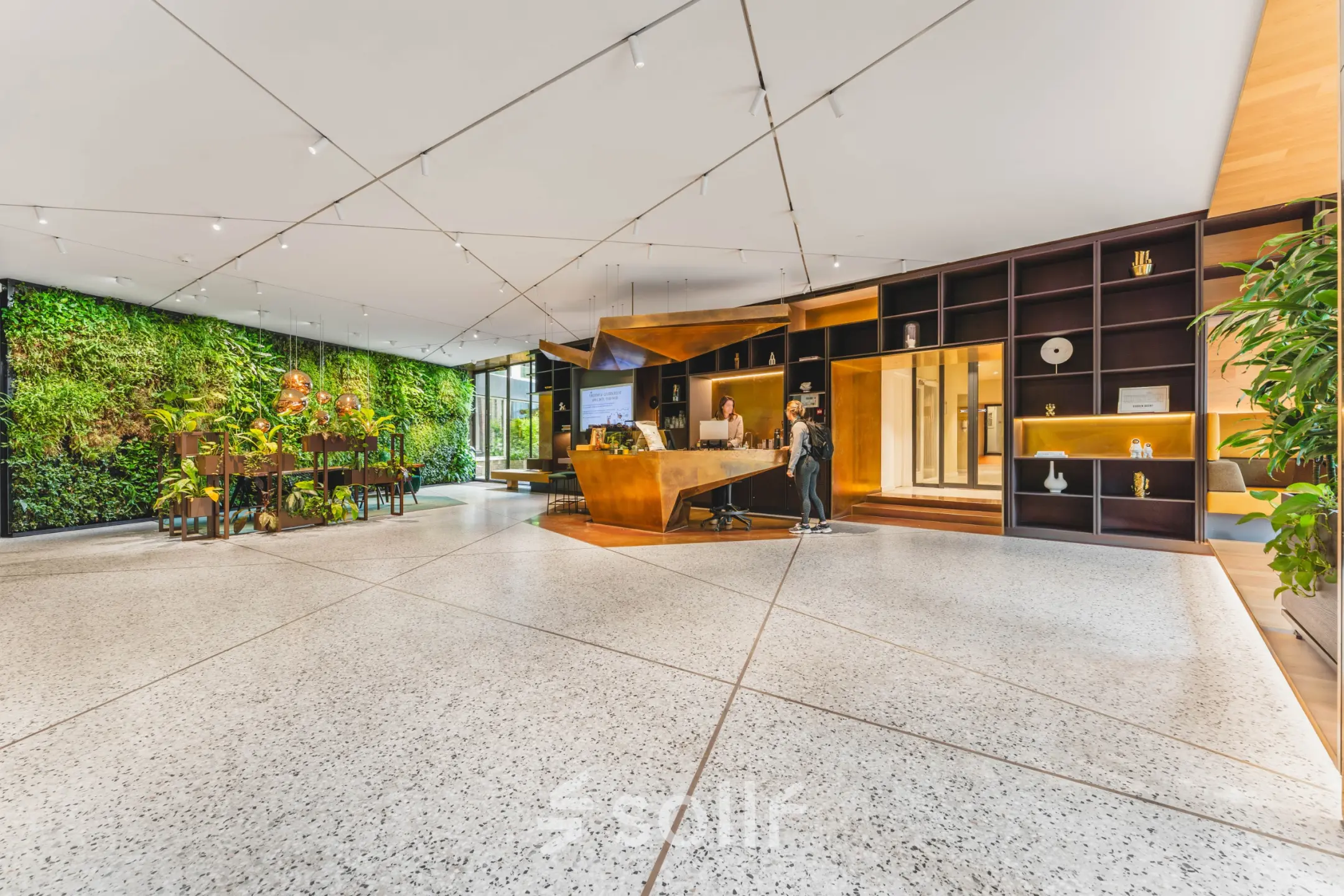 Modern reception area at office space rental on Herengracht 471, Amsterdam Center, featuring a green wall and sleek furnishings. Two individuals engaged in reception tasks.