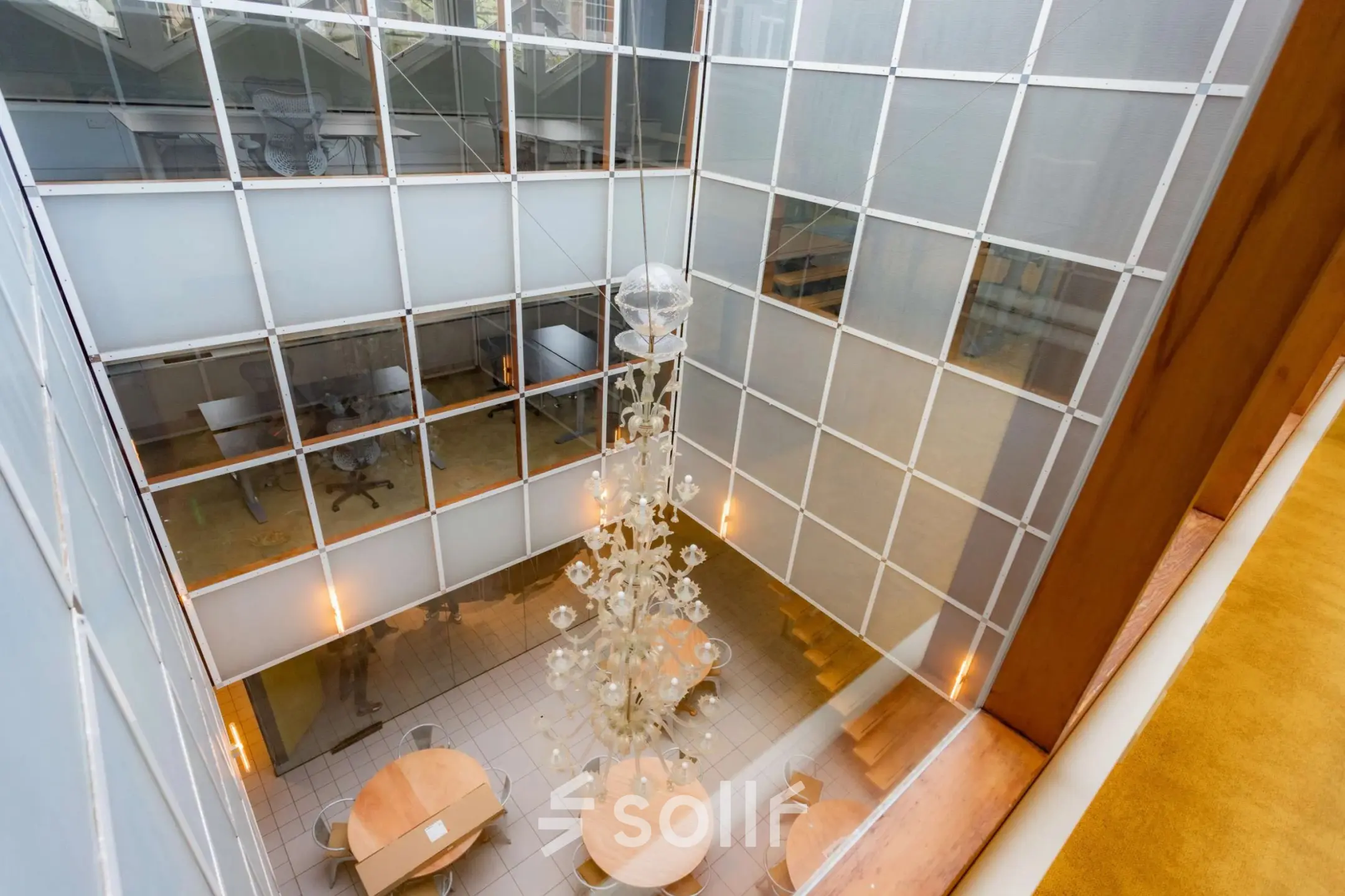 A modern, bright atrium with circular tables and a large chandelier, perfect for office space rental in Amsterdam Center.