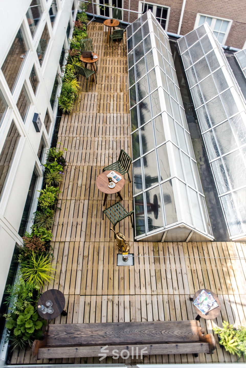 Rooftop terrace of the office located at Muiderstraat 1, Amsterdam Center. Features wooden decking, greenery, tables and chairs ideal for casual meetings or breaks. A unique spot for office space rental.