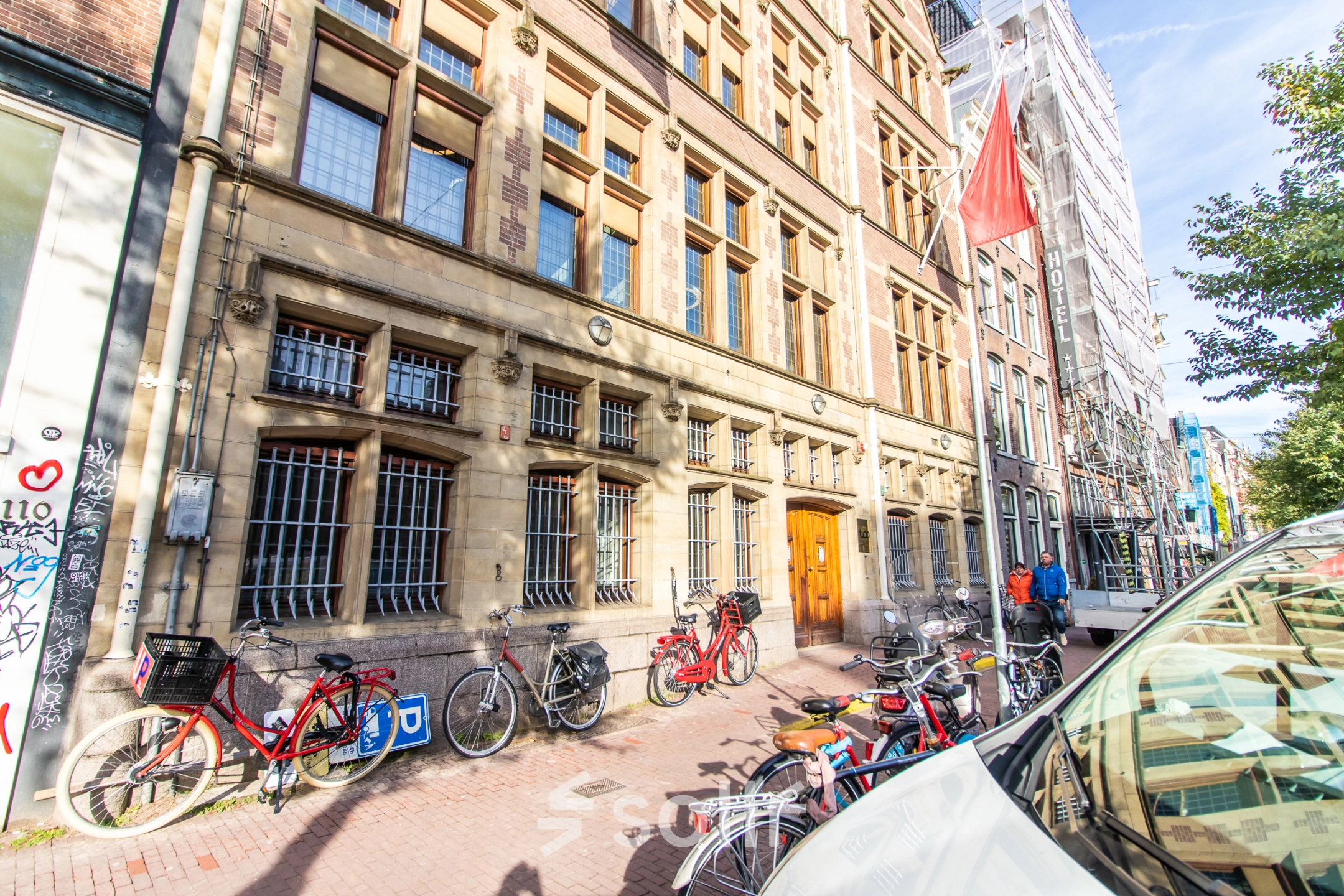 Exterior view of an office building located at Nieuwezijds Voorburgwal 104-108 in Amsterdam Center, featuring bicycles parked along the sidewalk and people walking by.