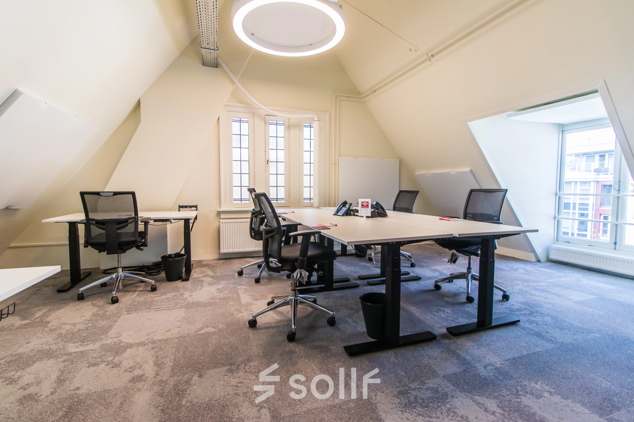 Bright office space for rent in Amsterdam Center, showcasing a furnished area with desks and chairs under a unique circular light fixture.