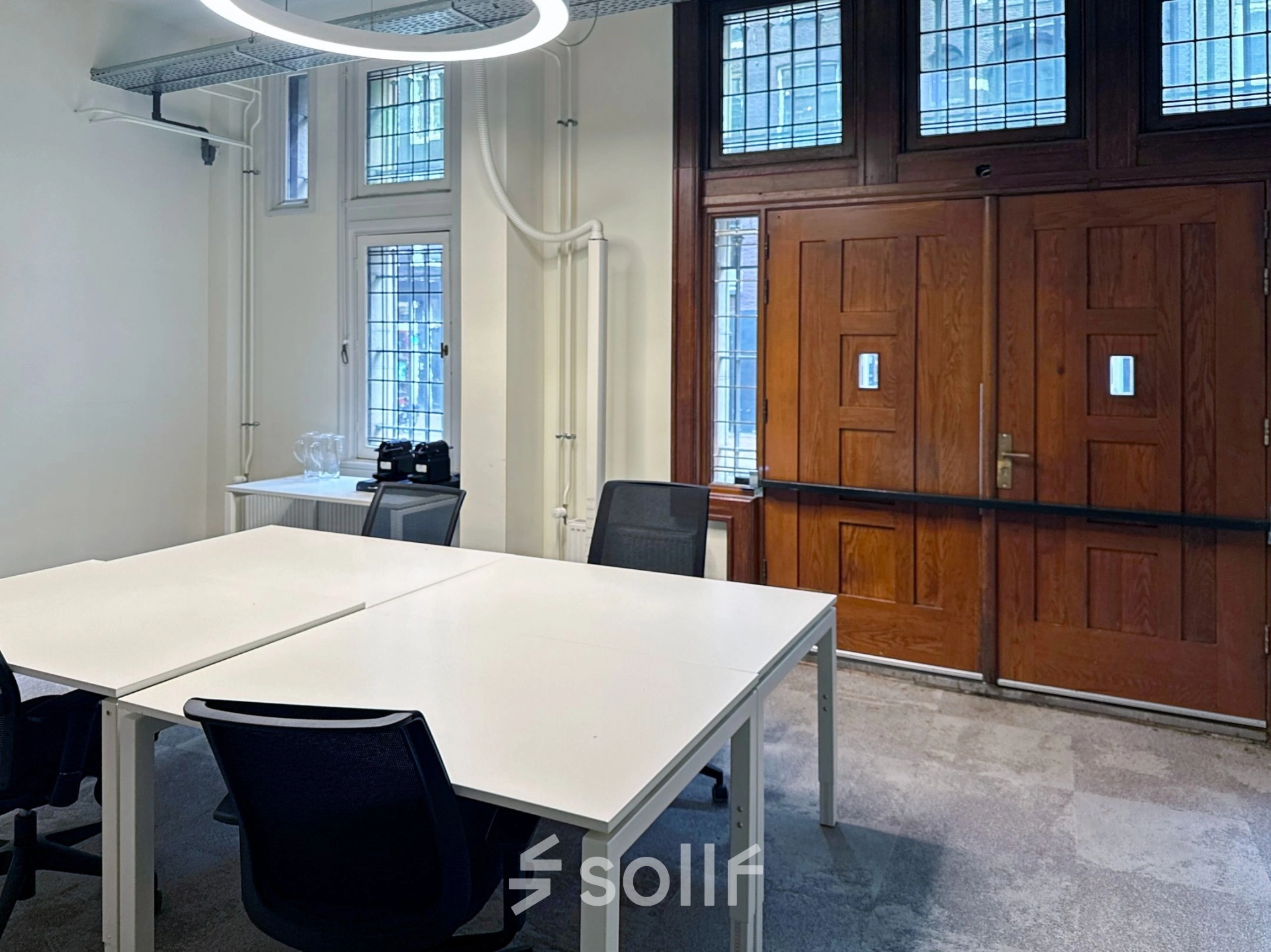 Interior view of an Amsterdam office space with modern desks and chairs near a wooden door, available for rent at Nieuwezijds Voorburgwal 104-108.