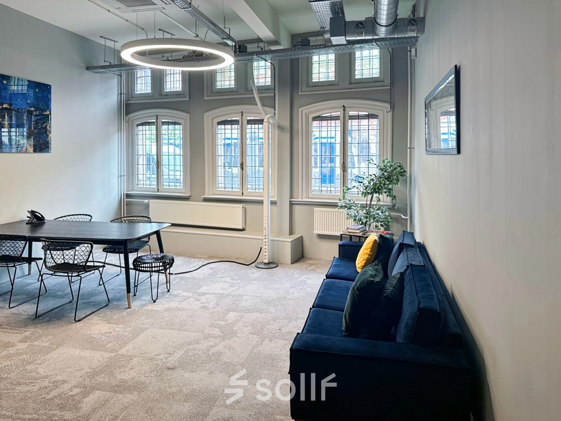 Bright office space in Amsterdam Center with modern furnishings, featuring a large table and seating area under stylish lighting. Perfect for office space rental on Nieuwezijds Voorburgwal.