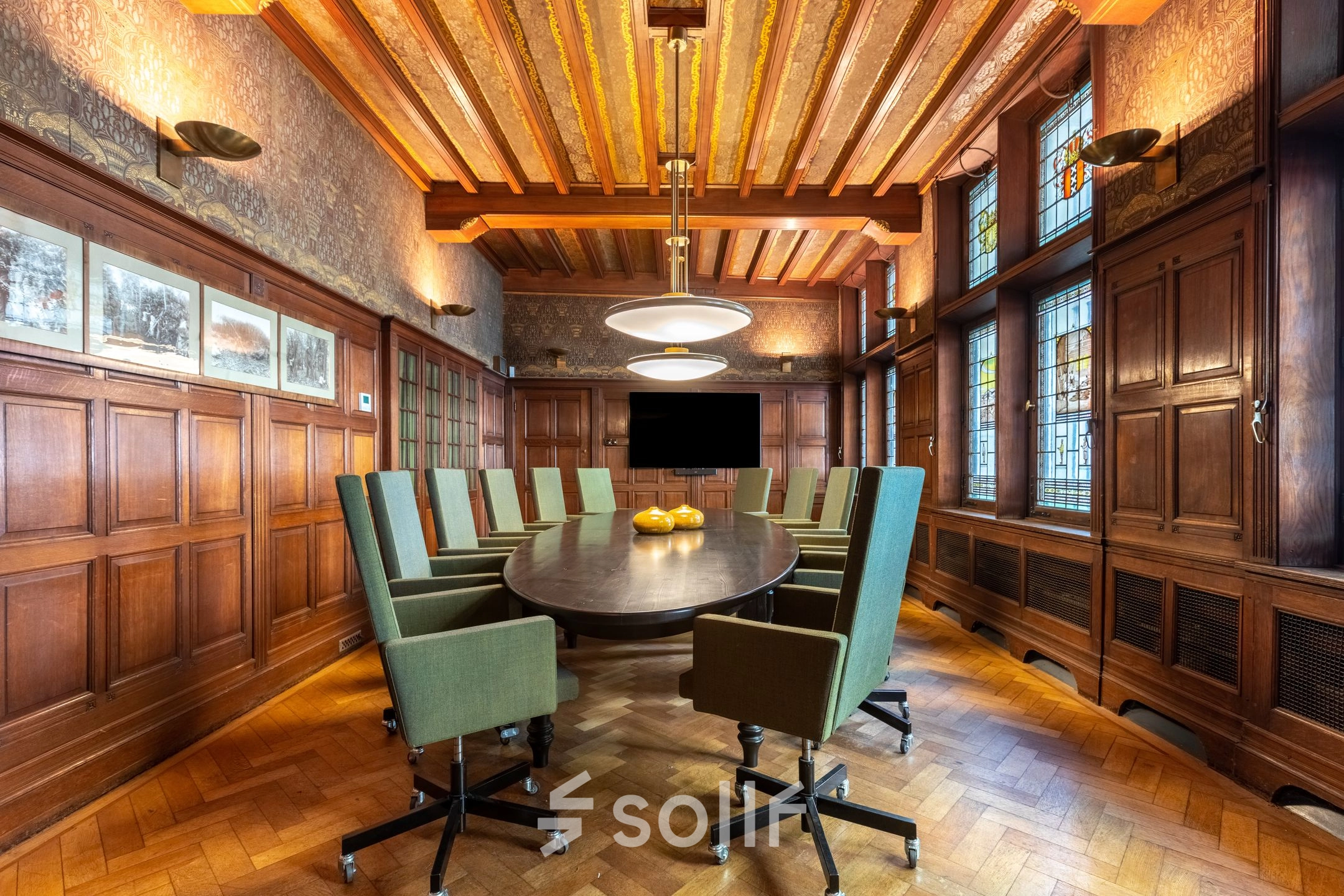 Charming conference room with wood paneling, featuring a large oval table surrounded by green upholstered chairs, ideal for office space rental in Amsterdam Center.