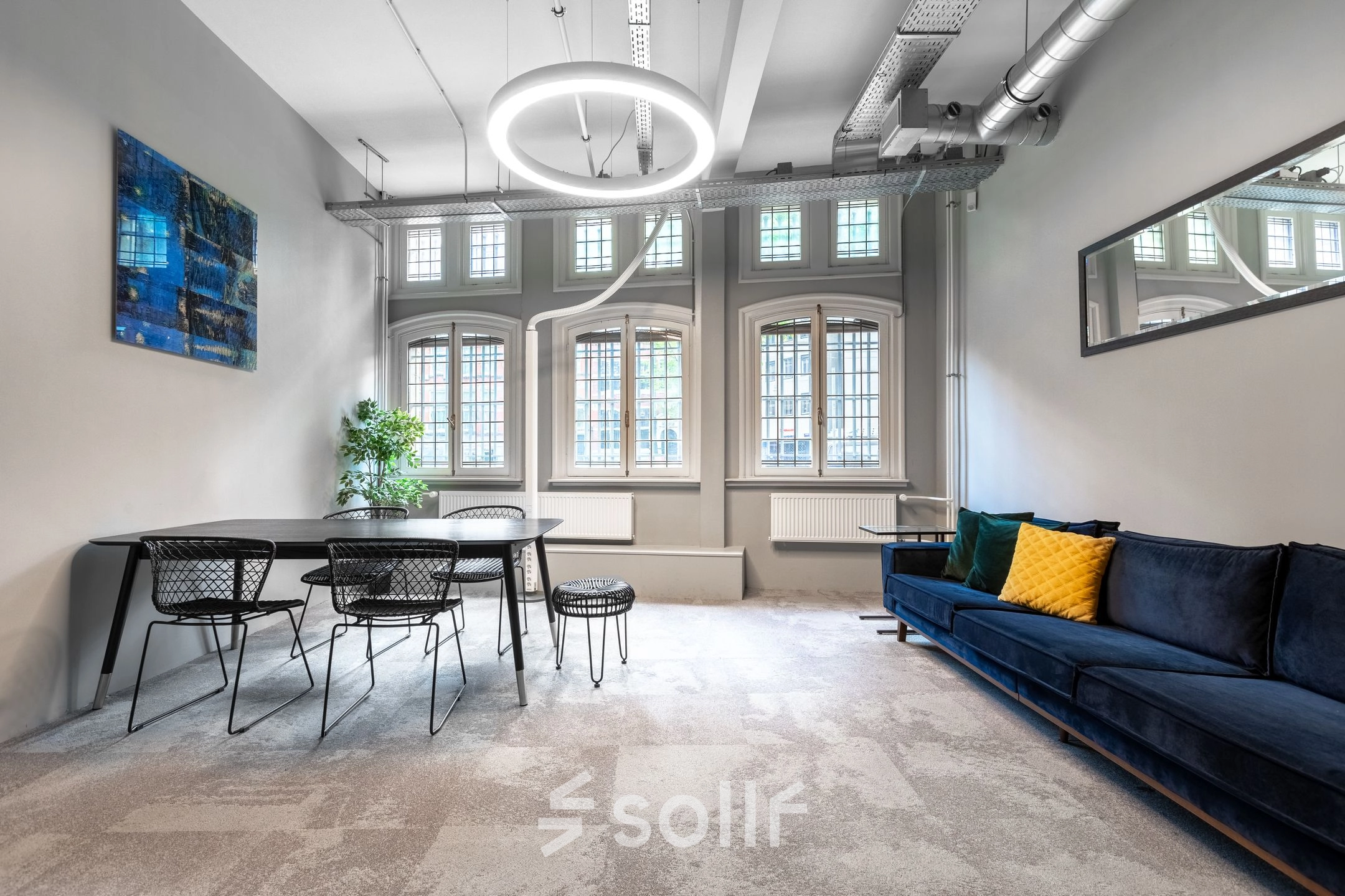 Bright office space for rent at Nieuwezijds Voorburgwal 104-108 in Amsterdam Center, featuring a modern design with a table, chairs, and a sofa under large, arched windows.