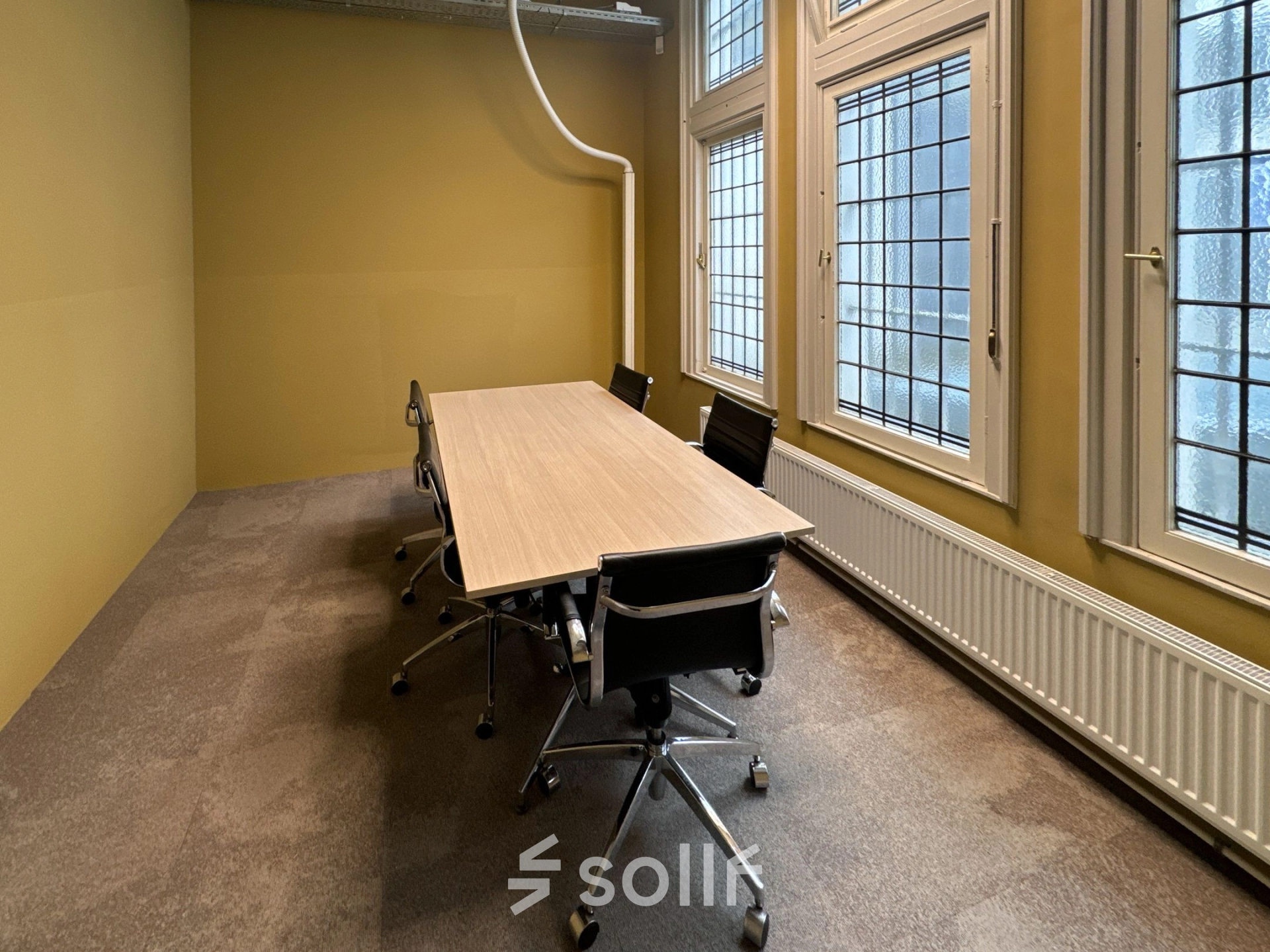 Furnished office space with a long wooden table and six chairs by large windows, available for rent at Nieuwezijds Voorburgwal 104-108 in Amsterdam Center.
