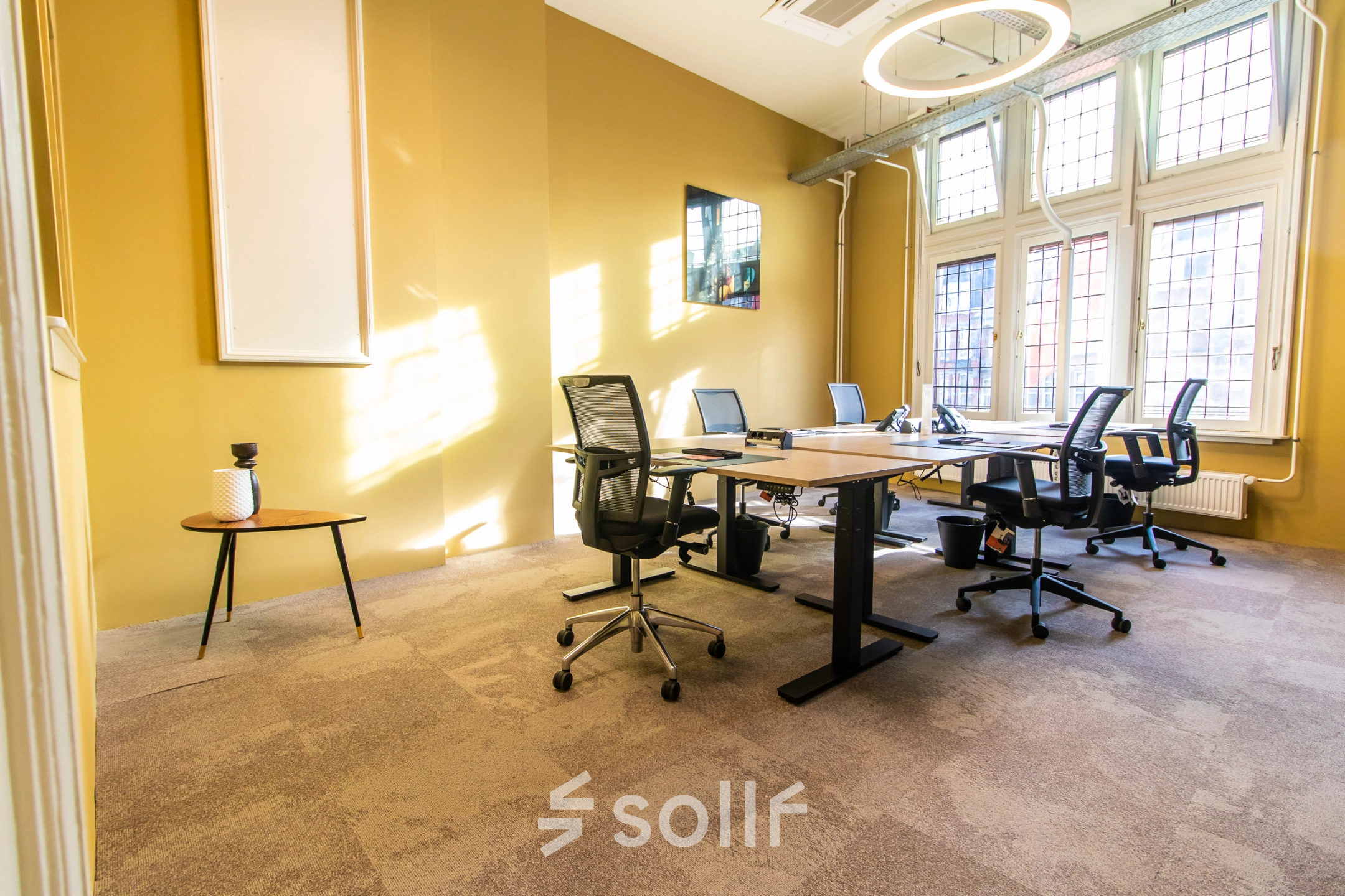 Bright office space with four workstations, modern chairs, and a small side table near large windows at Nieuwezijds Voorburgwal 104-108, ideal for office space rental in Amsterdam Center.