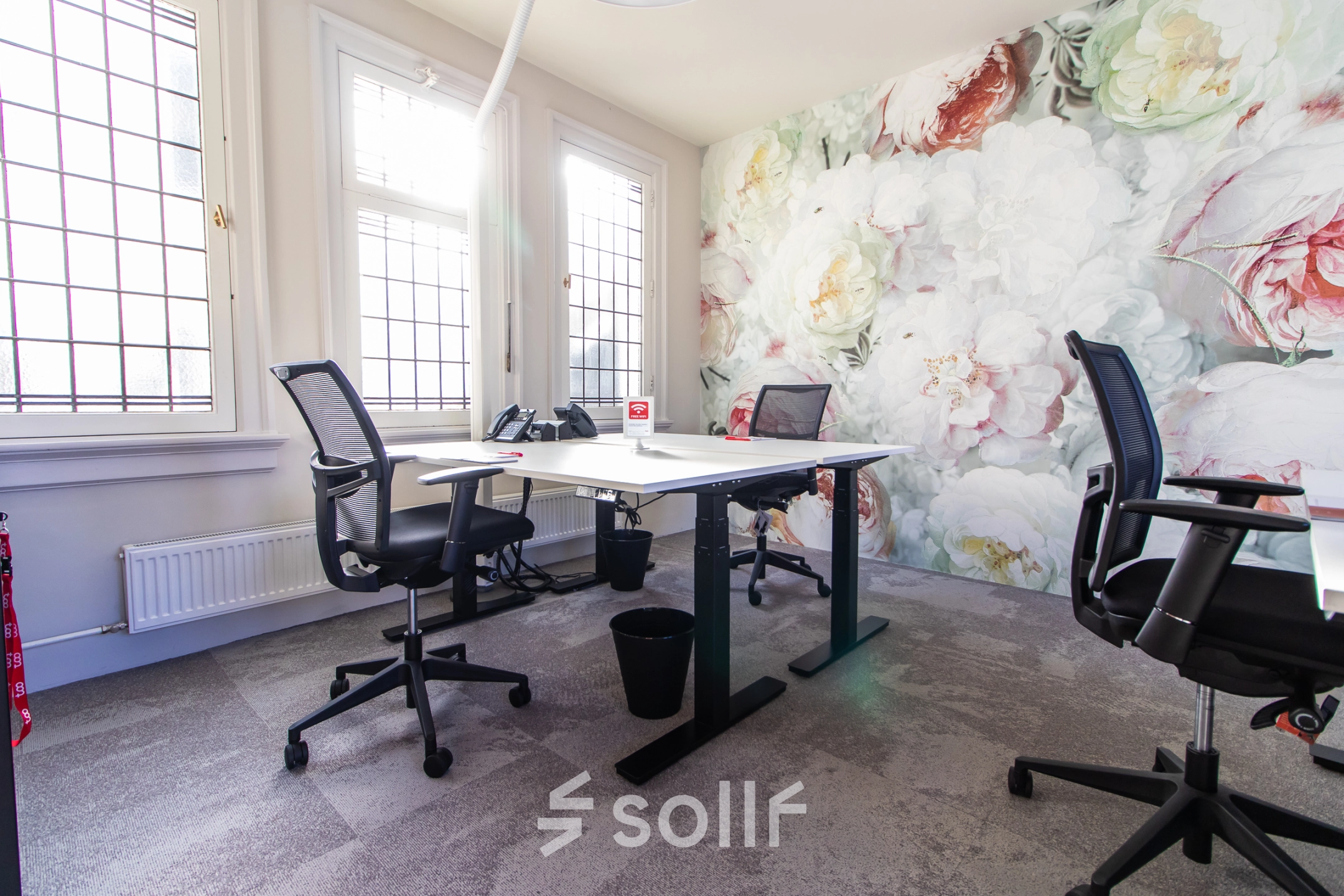 Bright office space with modern desks, ergonomic chairs, and a floral feature wall, perfect for rent office space in Amsterdam Center.