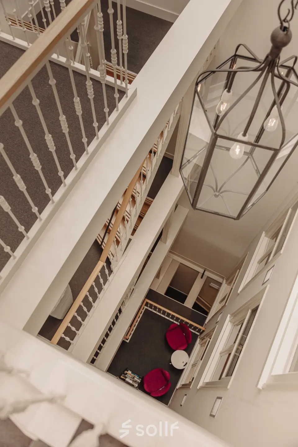 Interior view of an office space rental at Prins Hendrikkade 14, Amsterdam Center, featuring a multi-story staircase with modern lighting and seating area with pink chairs.