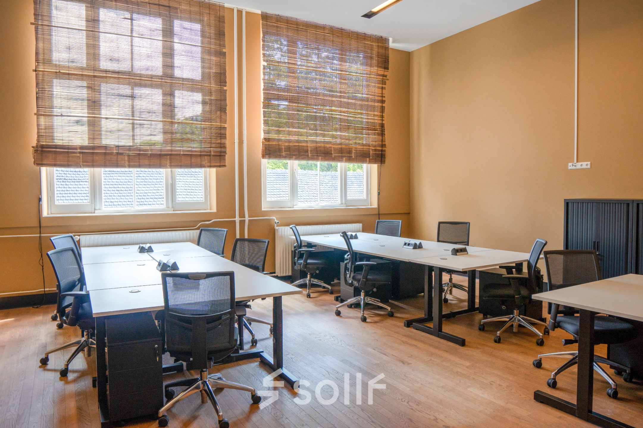 Bright office space with multiple desks and chairs, large windows with blinds, located at Raamplein 1 in Amsterdam Center. Ideal for office space rental.