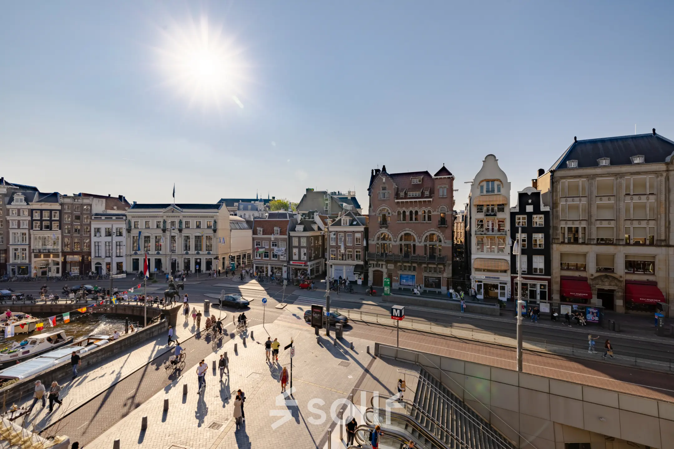 View of Rokin 117, Amsterdam Center, showcasing historic buildings under a bright sun with people walking on the street below.