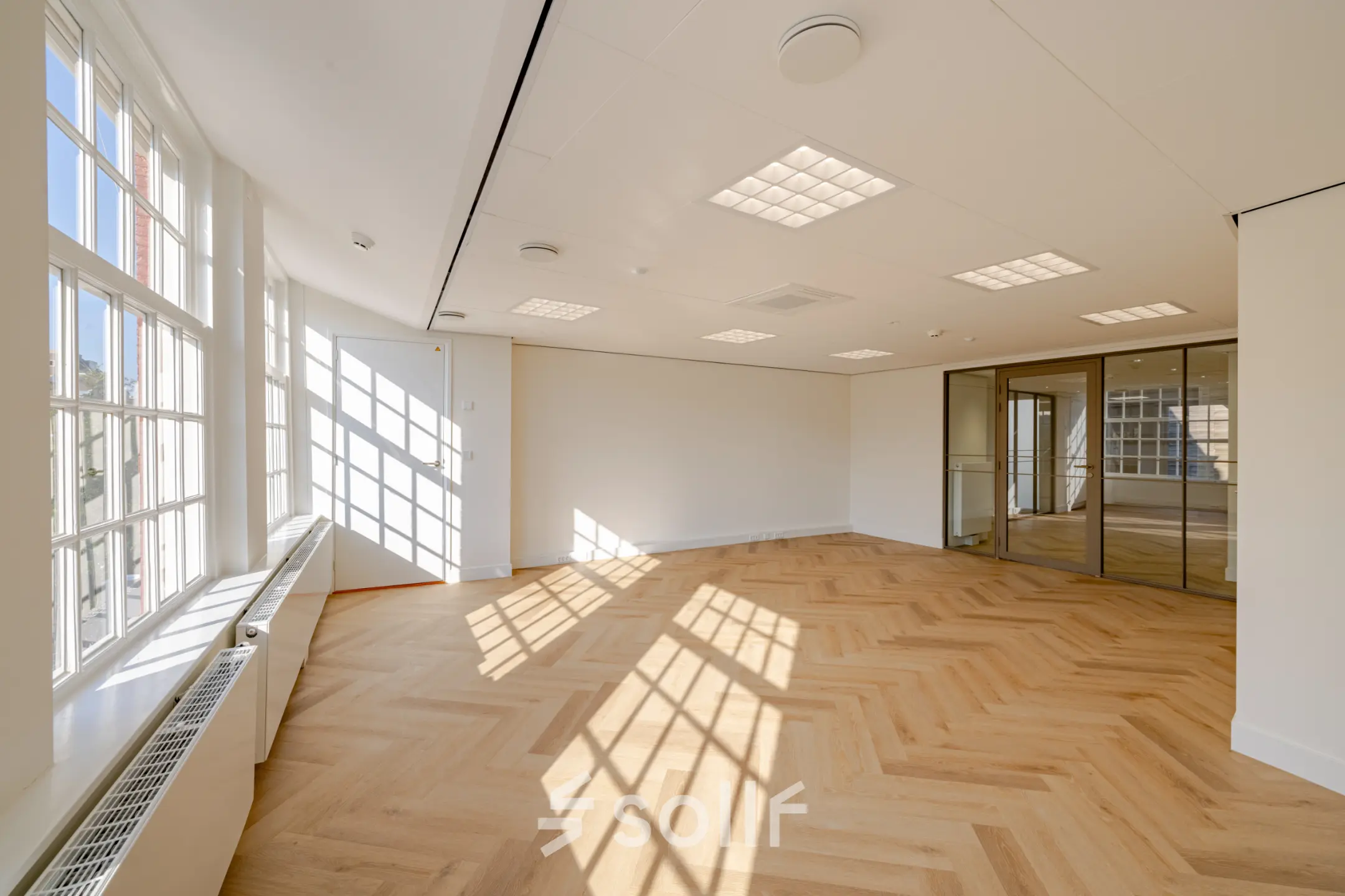 Bright and spacious office space with large windows and wooden flooring at Rokin 117 117, ideal for office space rental in Amsterdam Center.