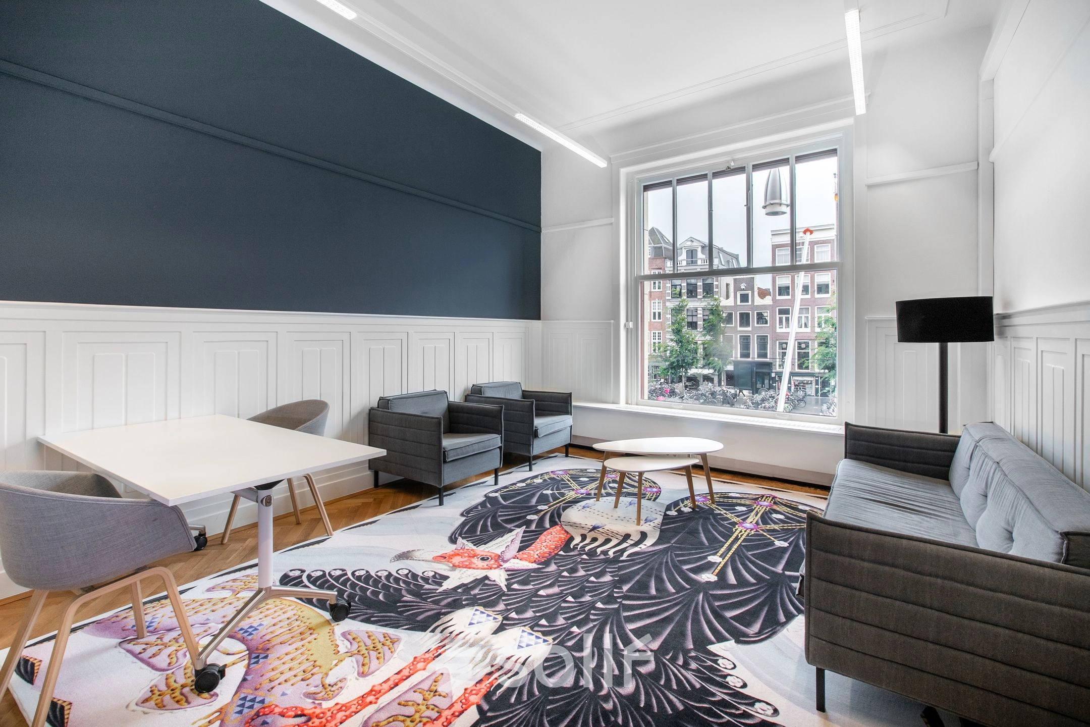 Modern office space rental at Rokin 92-96, Amsterdam Center, featuring contemporary furnishings with a vibrant rug and city views. Ideal office to rent for creative professionals.