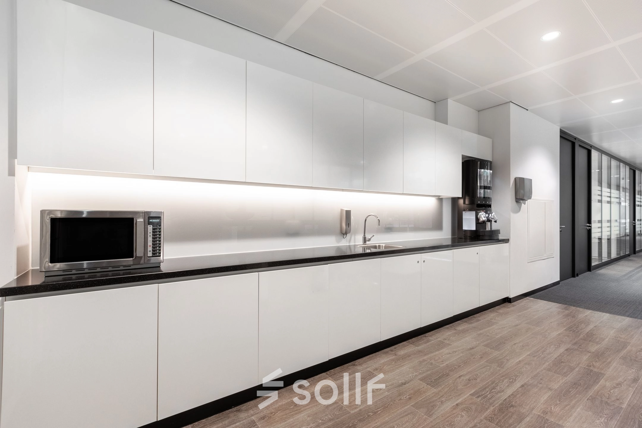 Modern office kitchen area at Rokin 92-96, Amsterdam Center, ideal for office space rental, featuring sleek white cabinets, a microwave, and a coffee machine.
