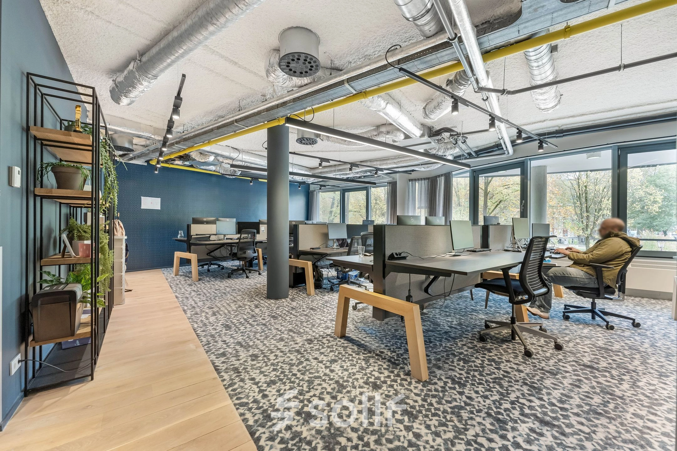 Bright office space at Stadhouderskade 55, Amsterdam Center, featuring several workstations and modern decor, available for rent. A person is seated and working at a desk.