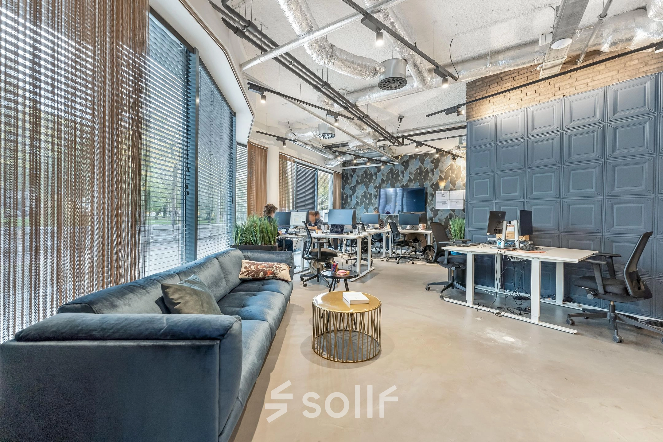 Modern office space at Stadhouderskade 55 in Amsterdam Center with employees working at computers and a seating area with a sofa and table. Ideal for office space rental.