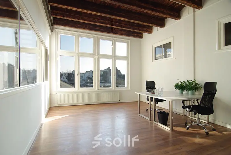 Bright office space with two desks and chairs at Warmoesstraat 155, Amsterdam Center, featuring large windows and wooden floors, ideal for rent office space. The room is empty and ready for use.