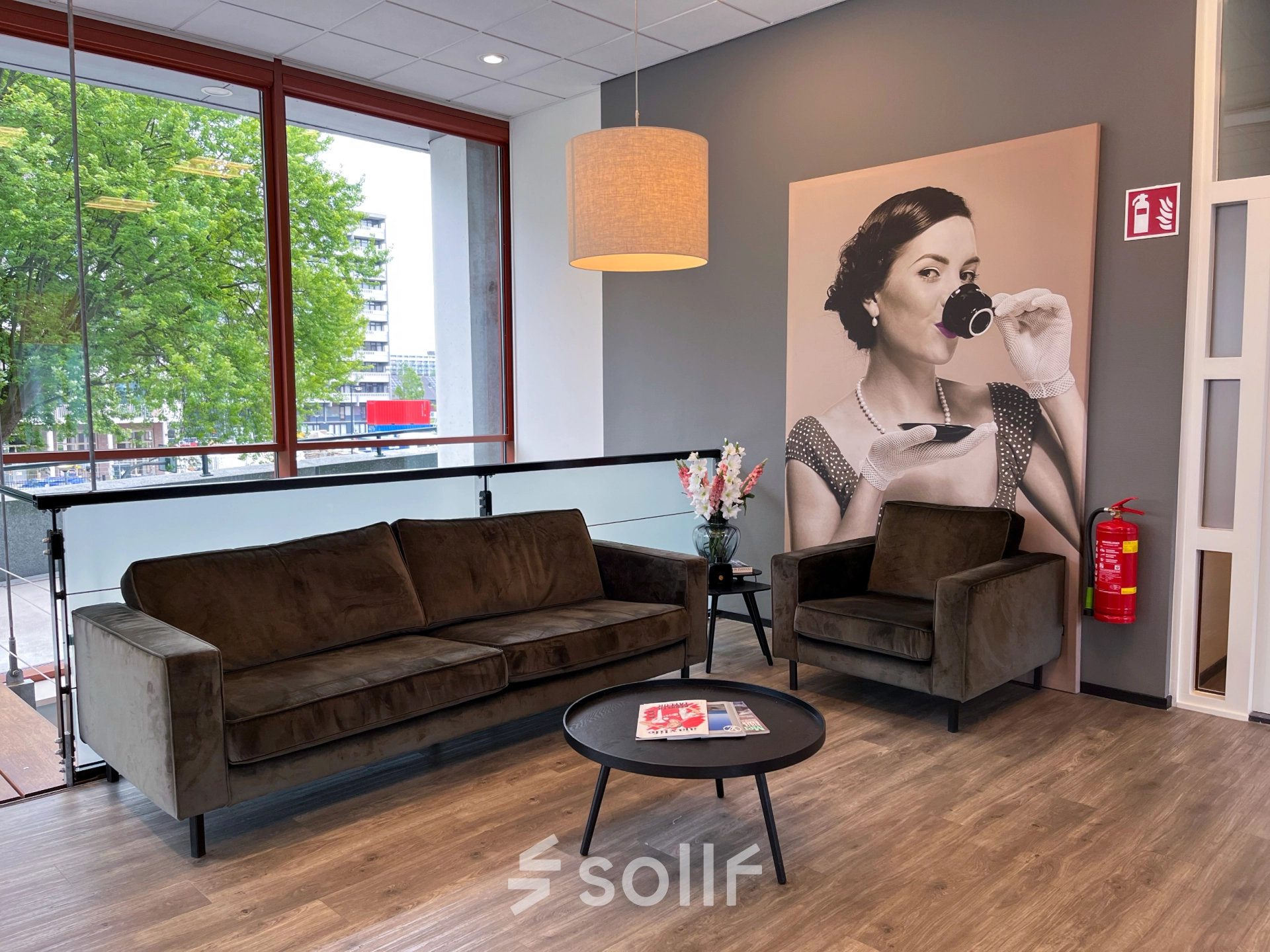 Stylish office lounge with a large window at Daalwijkdreef 47, Amsterdam Duivendrecht, perfect for office space rental. Features a cozy seating area with modern furniture and decorative art on the wall.