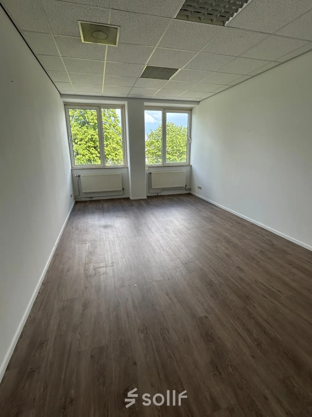 Empty office space at James Wattstraat 71, Amsterdam East, featuring large windows providing natural light and wooden flooring, ideal for office space rental.