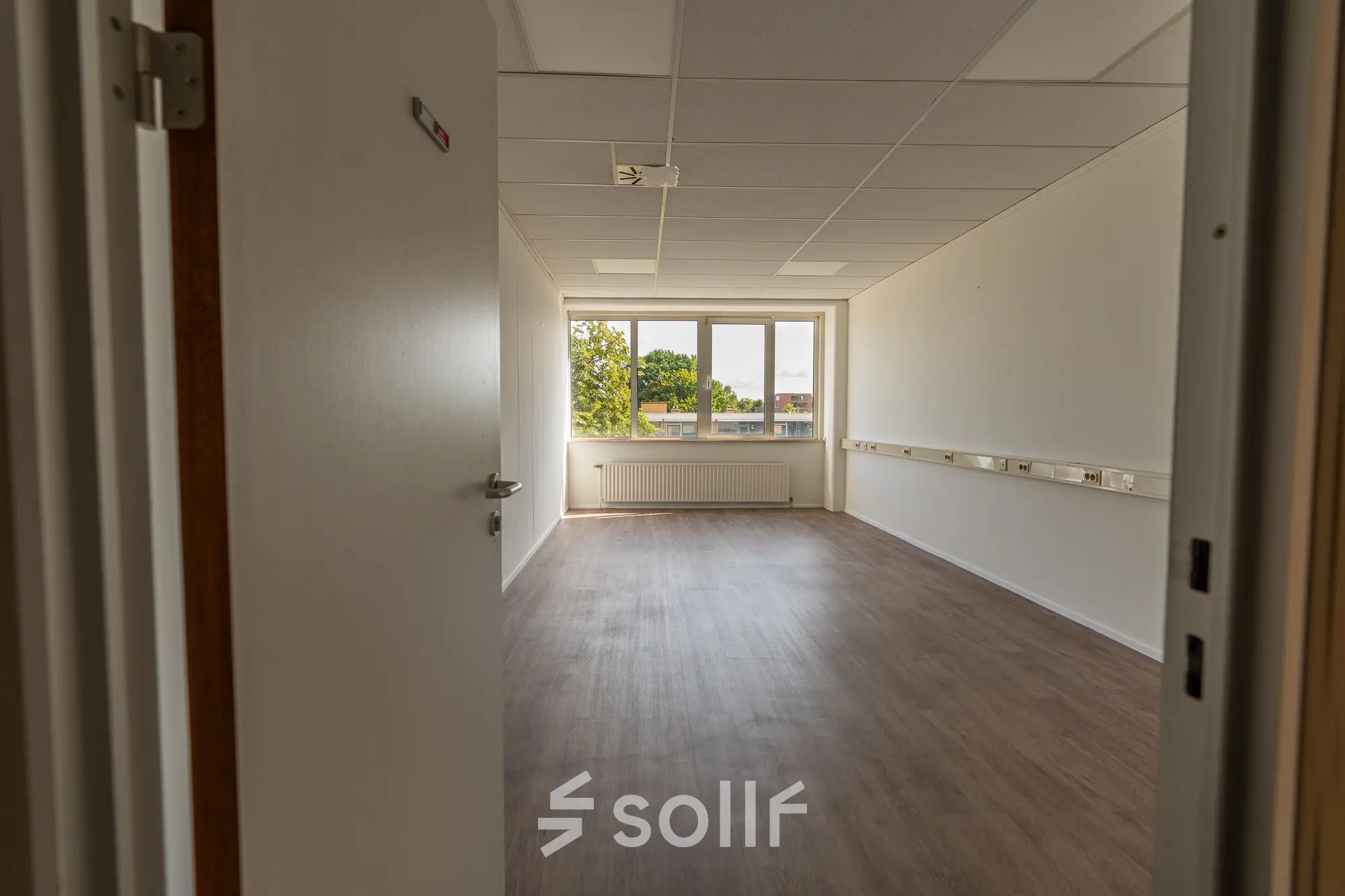 Unfurnished office space available for rent at James Wattstraat 71, Amsterdam East, featuring a bright room with wooden flooring and a large window.