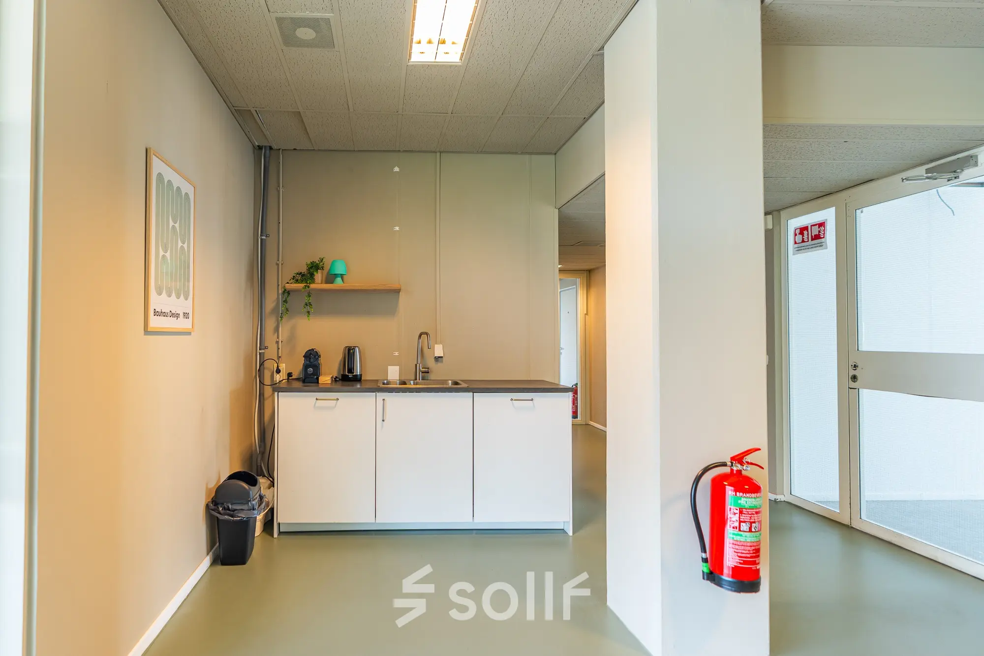 Compact pantry area in an Amsterdam East office space featuring a counter with a coffee machine and minimal decor.