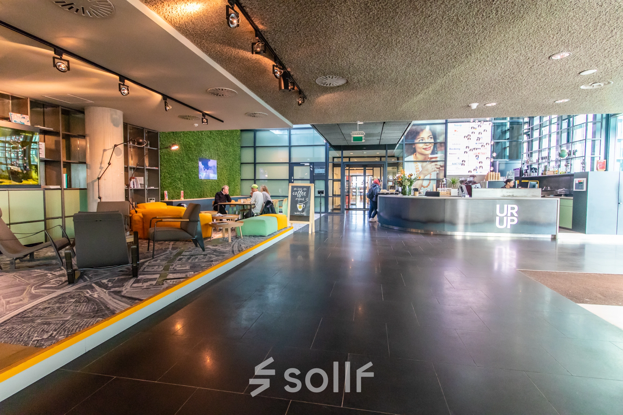 Spacious office lobby at Piet Heinkade 55, Amsterdam East, featuring modern furnishings and people engaging in business conversations, ideal for office space rental.