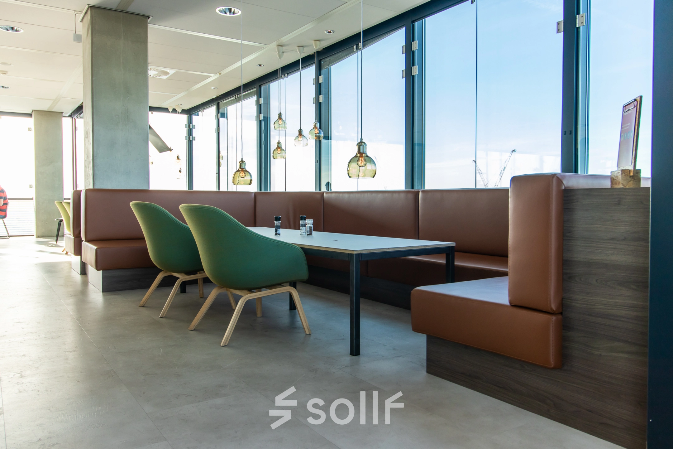 Modern office lounge area with large windows, green chairs, and brown leather seating at Piet Heinkade 55, ideal for an office space rental in Amsterdam East.