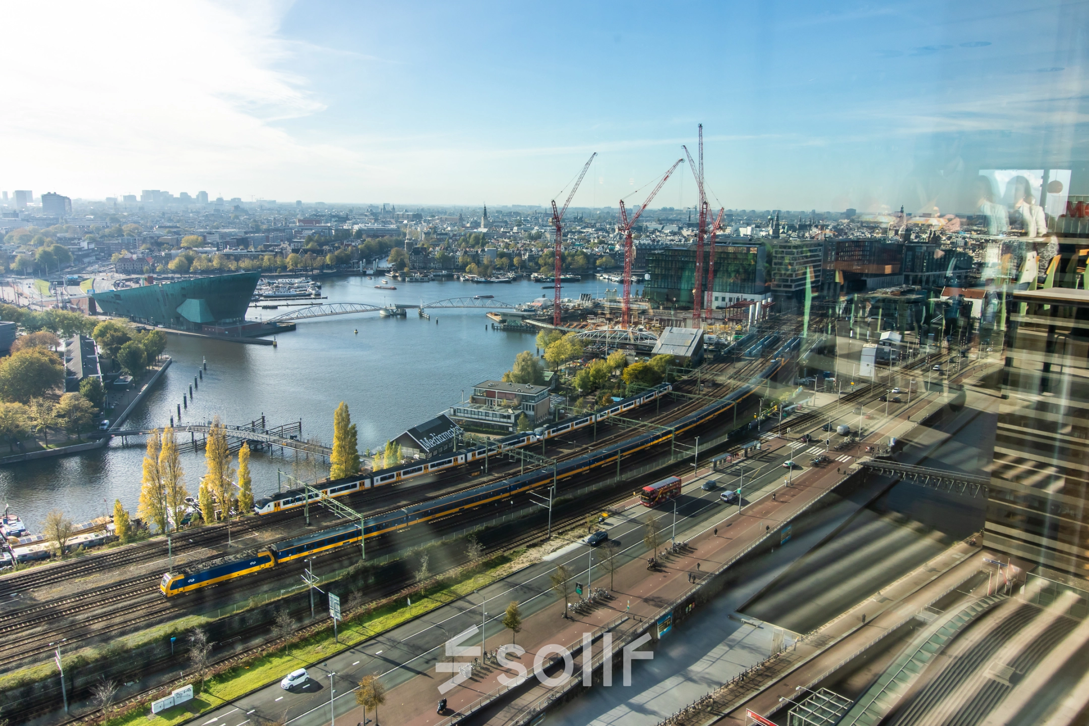 View from office to rent at Piet Heinkade 55, featuring Amsterdam East's skyline with a river, roads, and distant buildings.