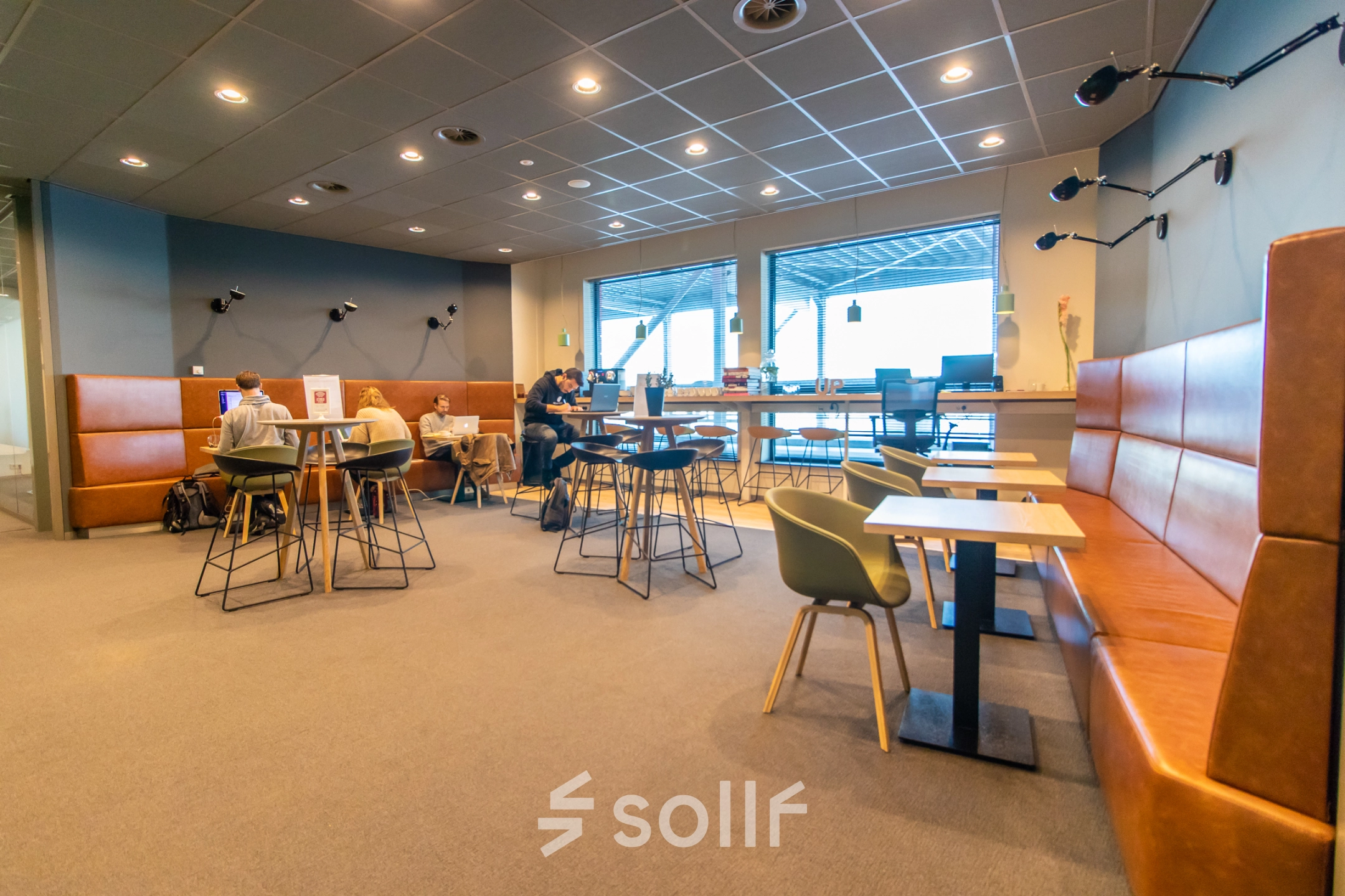Modern office space rental at Piet Heinkade 55 in Amsterdam East, featuring stylish furniture and individuals engaged in meetings and work discussions.