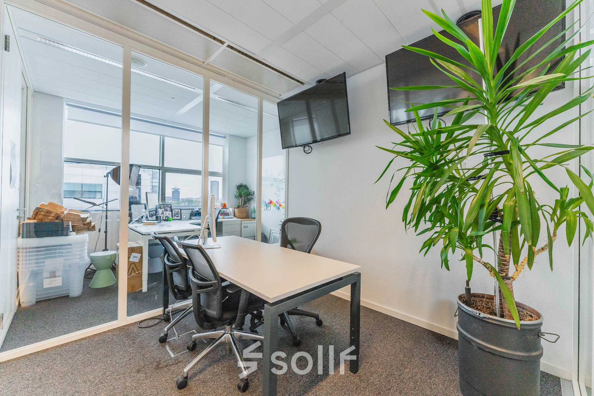 Furnished office space at Piet Heinkade 95B, Amsterdam East, featuring a conference table, chairs, a wall-mounted TV, and large windows for natural light. Ideal office space rental option.