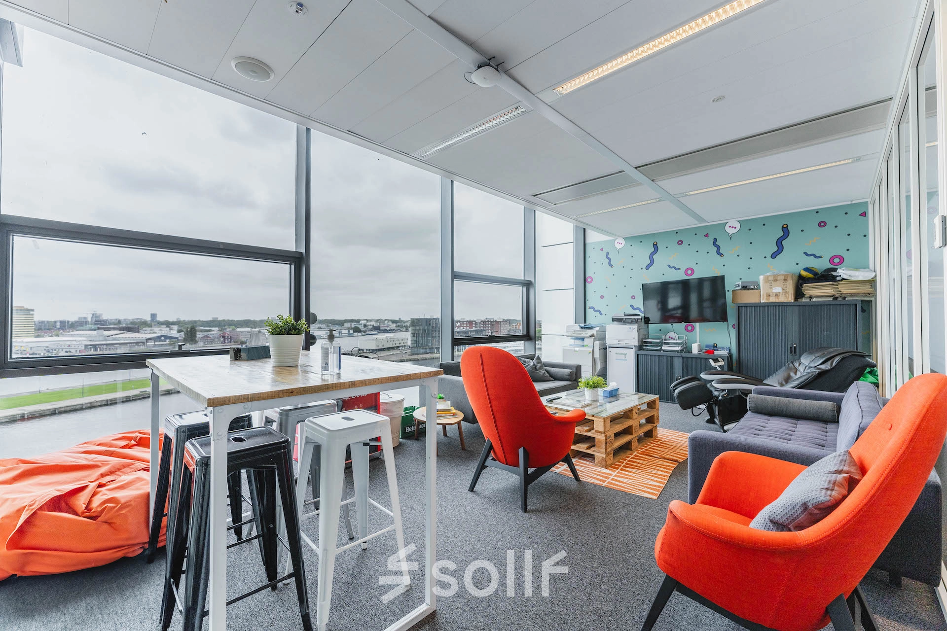 Furnished office space at Piet Heinkade 95B, Amsterdam East with vibrant seating, a wooden table, and large windows offering scenic views; perfect for office space rental.