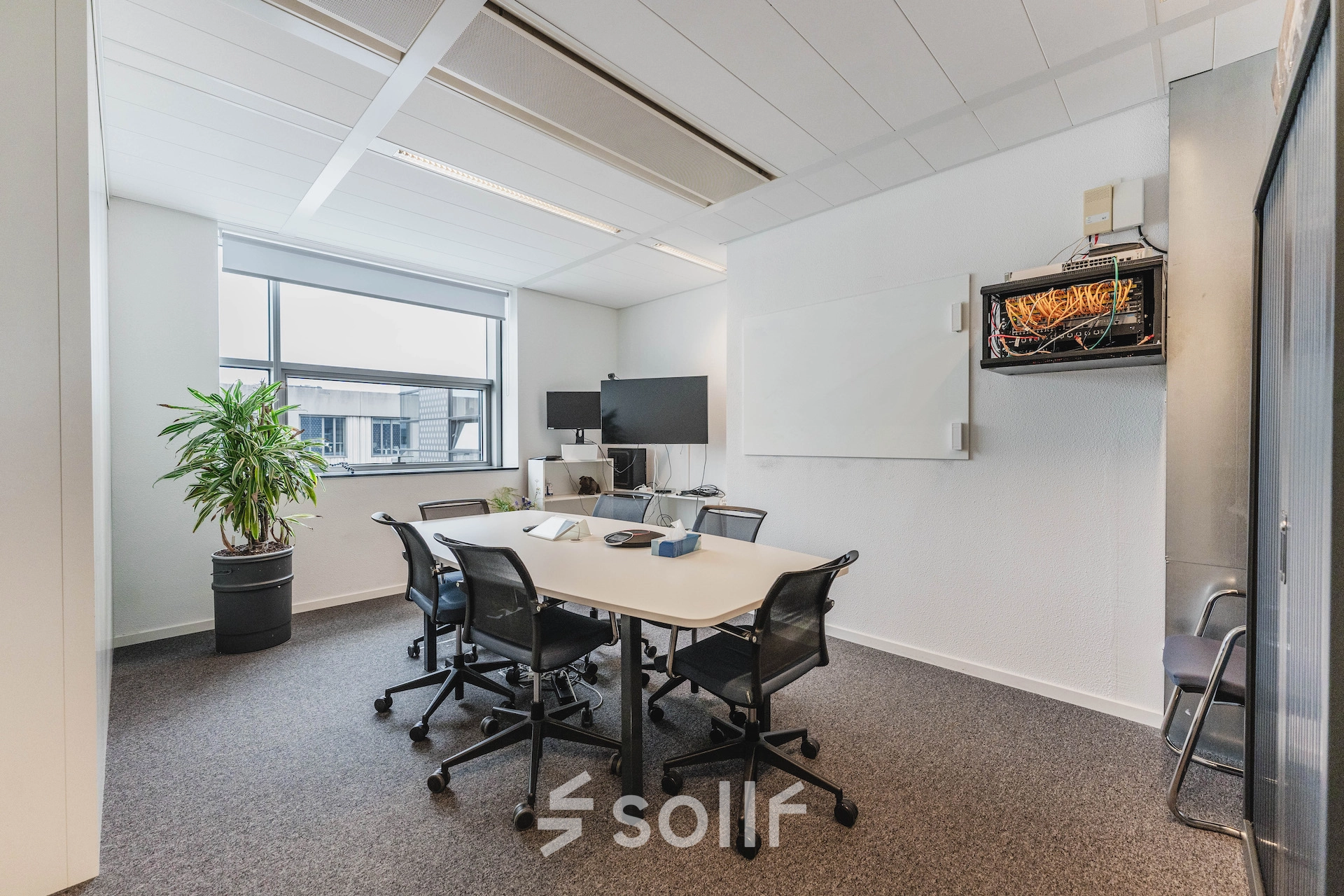 Modern office space at Piet Heinkade 95B, Amsterdam East, featuring a meeting table, chairs, and a large window with natural light. Ideal for office space rental.