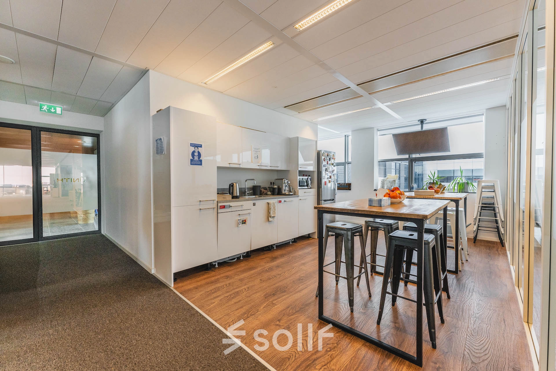 Modern office space in Amsterdam East at Piet Heinkade 95B with sleek wooden floors, a furnished area including a high table and stools, and a kitchenette perfect for office space rental.