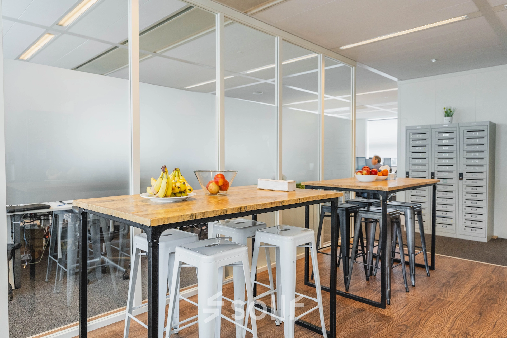 Modern office space at Piet Heinkade 95B, Amsterdam East, featuring high tables with stools, frosted glass walls, and trendy decor ideal for office space rental.