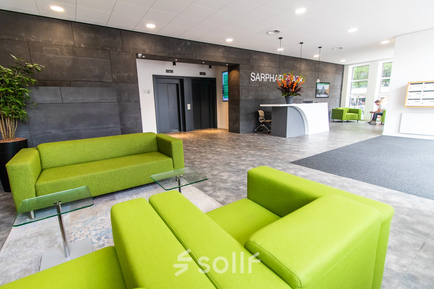Bright and welcoming office space rental in Amsterdam East, featuring vibrant green sofas, a modern reception area, and elevators. Ideal for businesses looking to rent office space at Rhijnspoorplein 10-38.