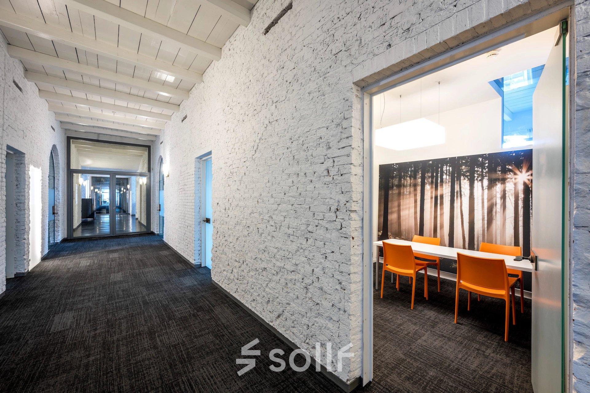 Interior hallway at Sarphatistraat 370, Amsterdam East, leading to a furnished office space with bright orange chairs and a forest-themed wall. Ideal office space rental with modern amenities.