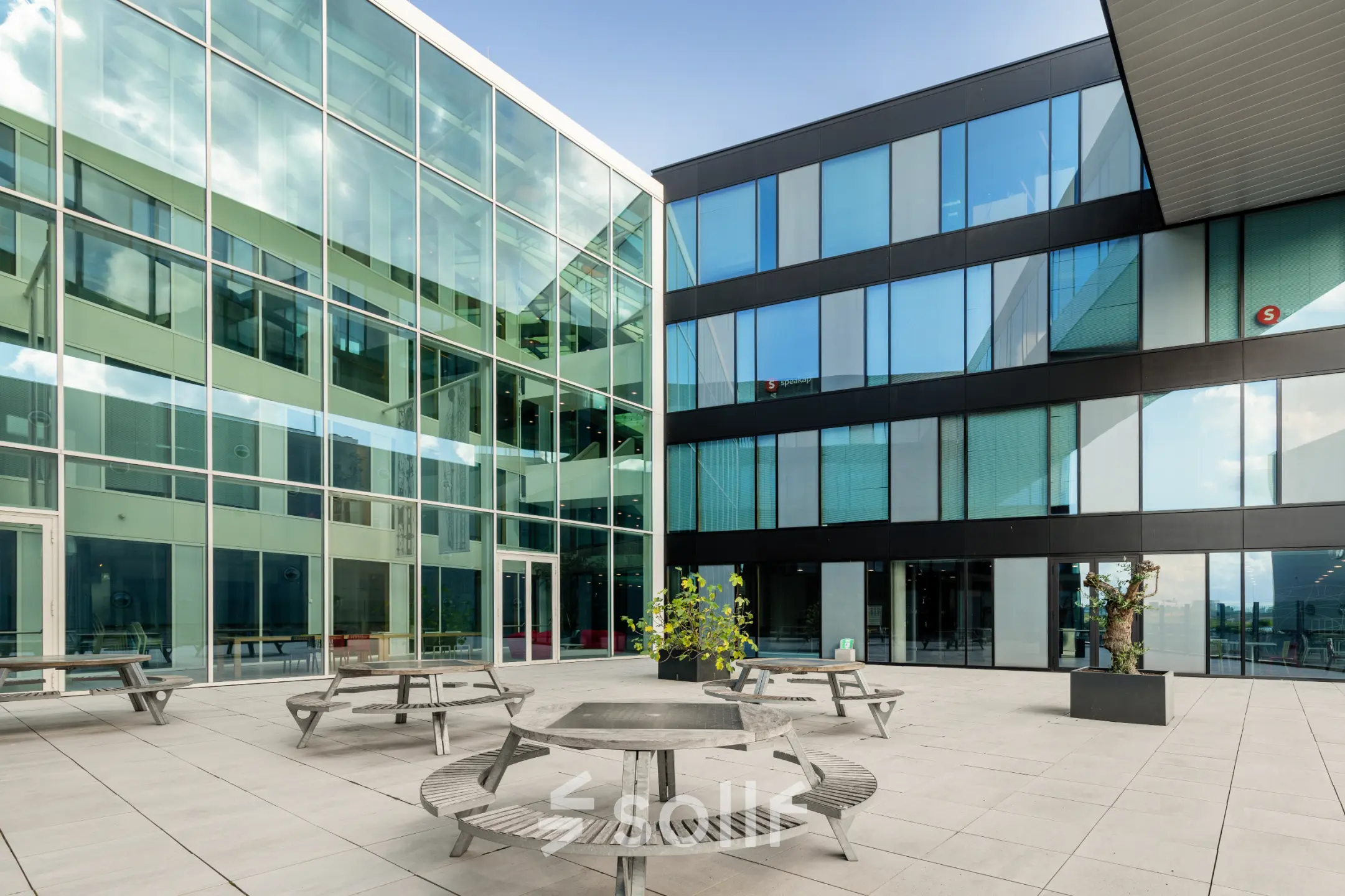 Exterior view of a modern office building at Pedro de Medinalaan 1-9, Amsterdam IJburg, featuring a spacious courtyard with bench seating. Ideal for office space rental.