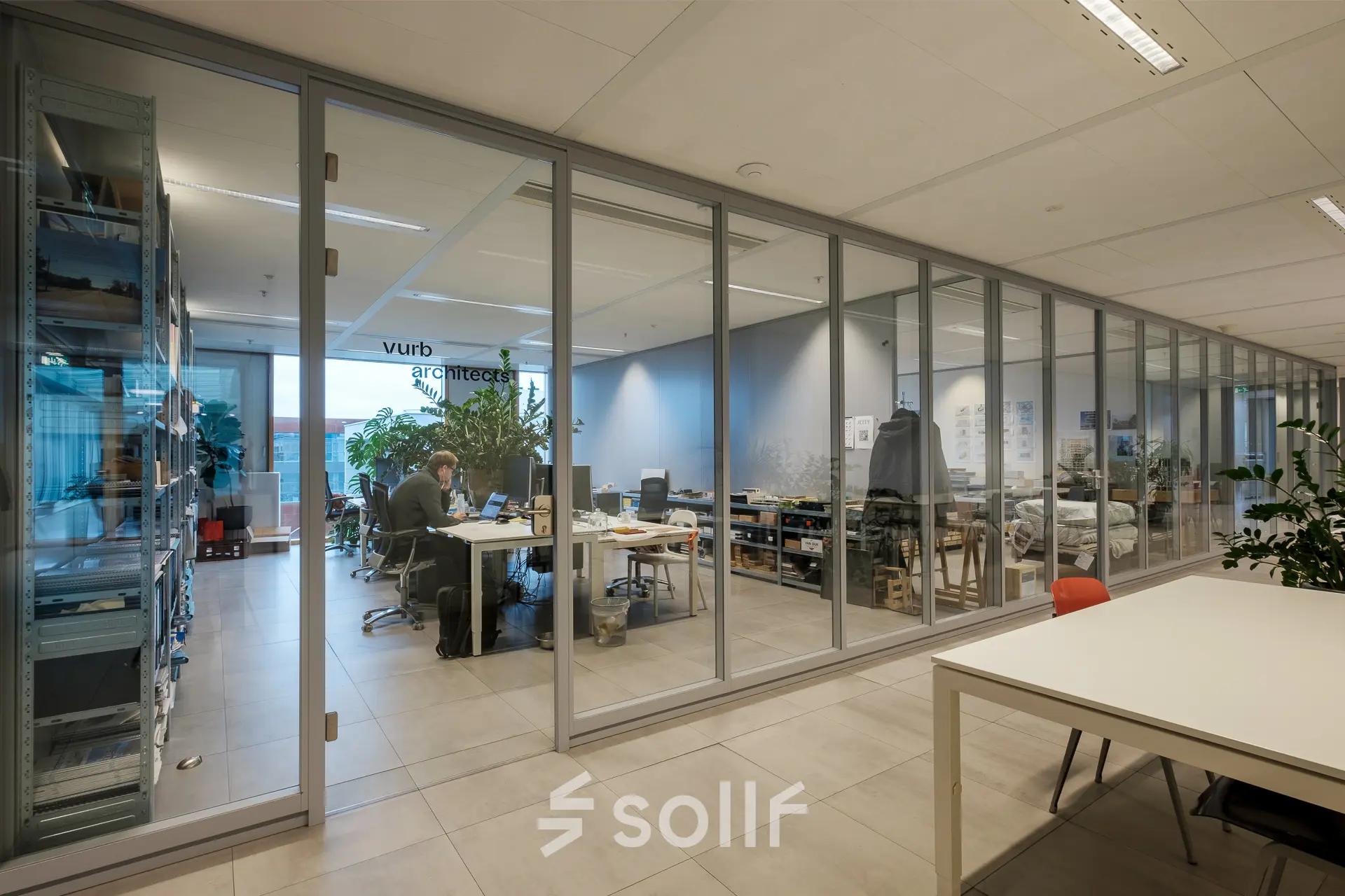 Modern office interior at Pedro de Medinalaan 7, Amsterdam IJburg, featuring glass partitions and a workspace with professionals engaged in business activities.