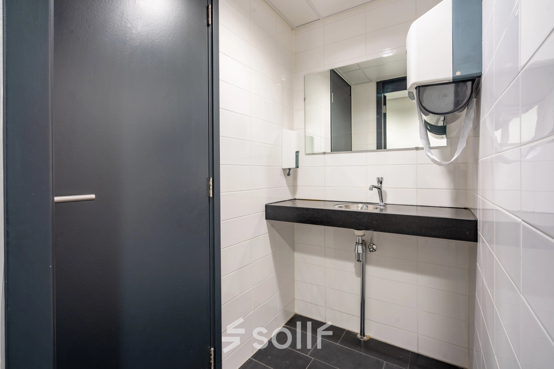 Modern restroom at an office for rent in Amsterdam New-West with a sleek black countertop and white tiled walls.