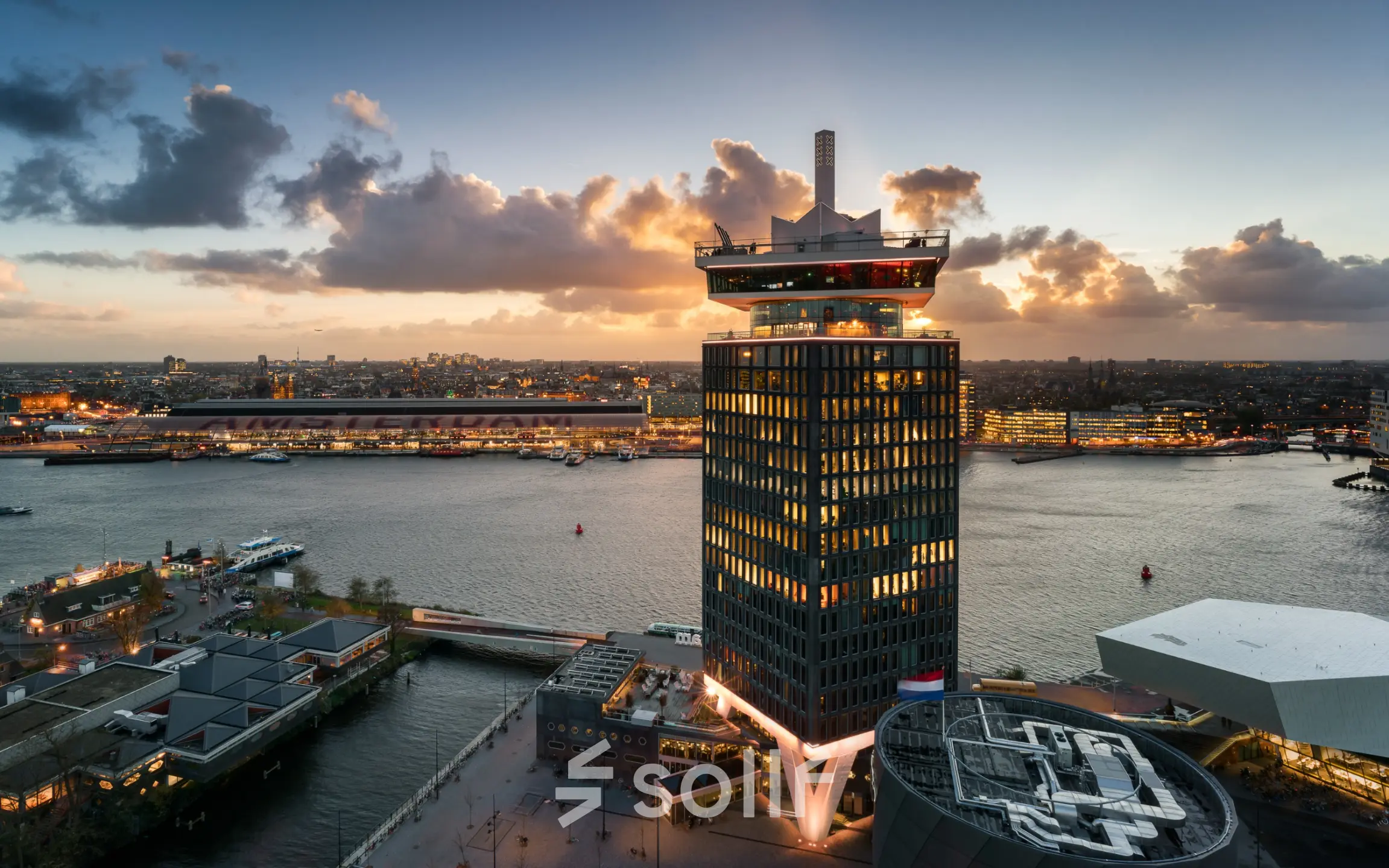 Aerial view of the striking office building at Overhoeksplein 1 in Amsterdam North, highlighting its modern architecture against a sunset backdrop over the water.