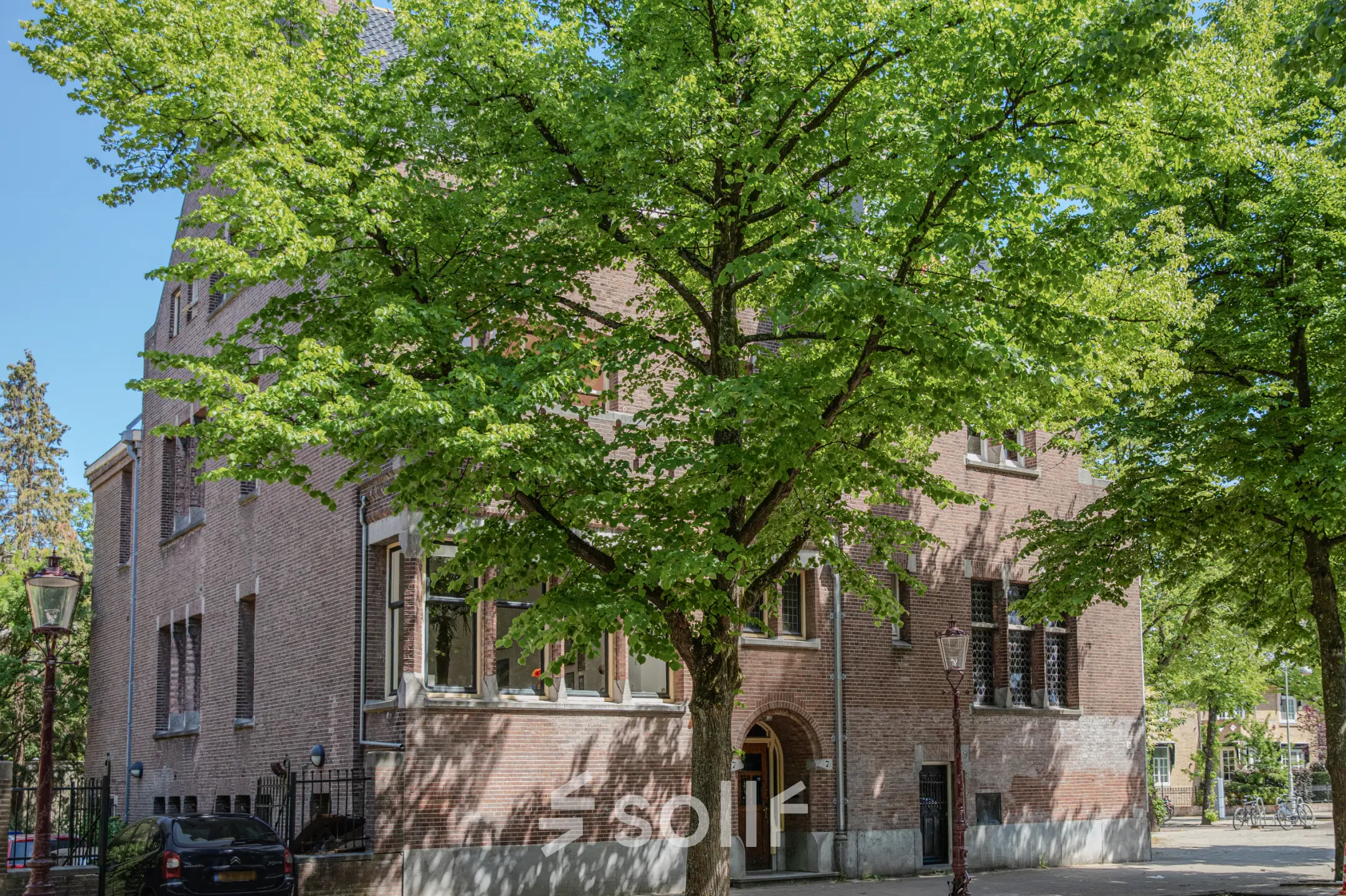 Exterior view of Emmalaan 7-9, Amsterdam Old South showcasing the brick office building surrounded by lush green trees, ideal for office space rental.