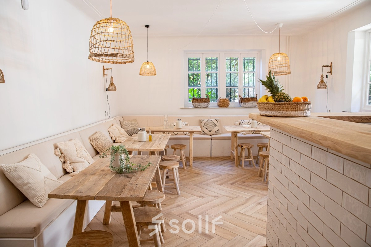 A cozy office to rent in Amsterdam Old South with wooden tables, cushioned benches, and natural light through large windows, perfect for work or meetings. Ideal for office space rental.