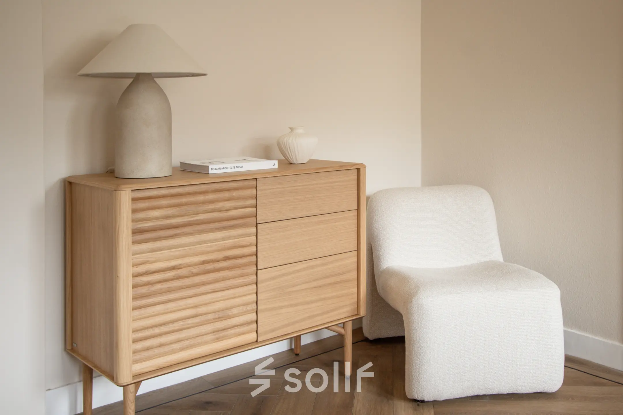 A cozy corner in an Amsterdam Old South office to rent, featuring a stylish wooden sideboard, a modern lamp, and a comfortable chair on a parquet floor.