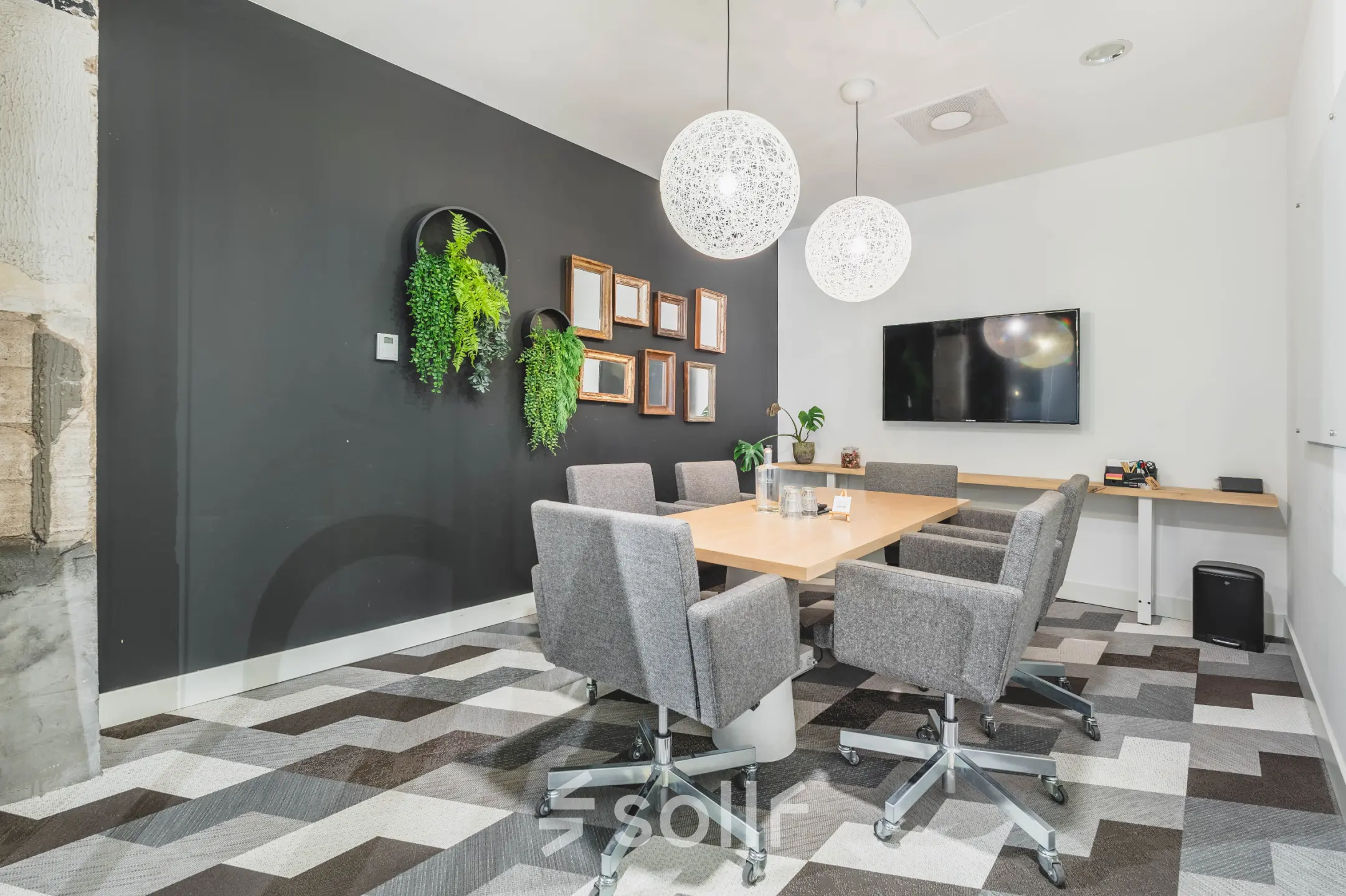 A modern conference room with a wooden table, grey chairs, wall-mounted TV, and decorative plants at Olympisch Stadion 24-28 in Amsterdam Old South, available for office space rental.