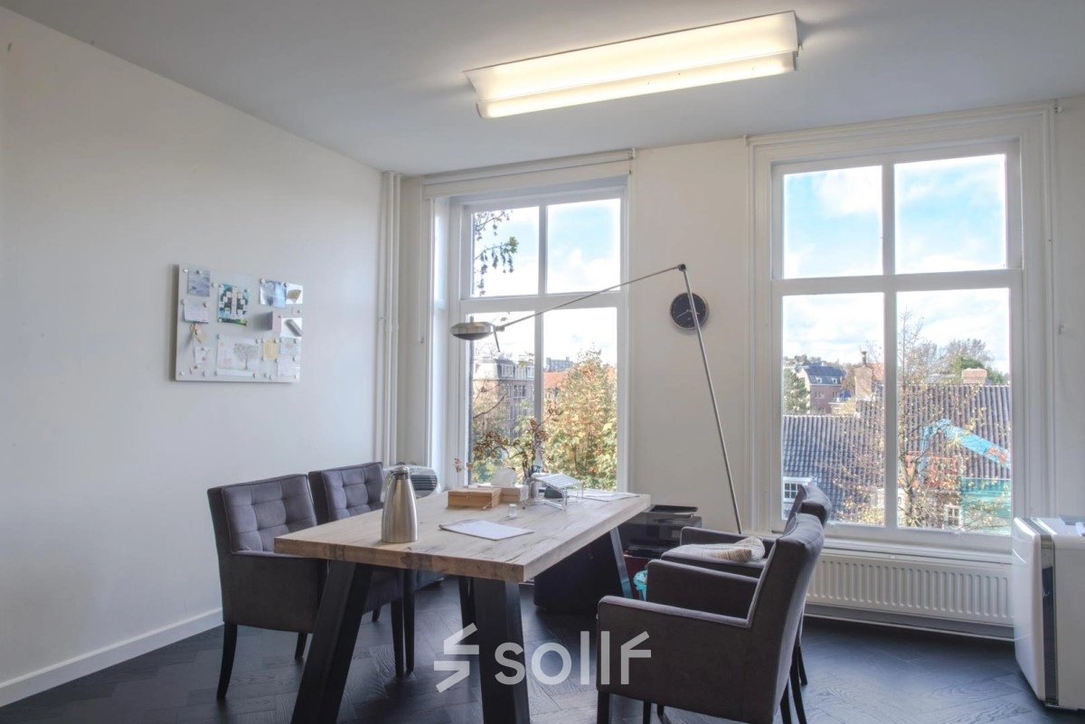 Furnished office space to rent at Sophialaan 21, Amsterdam Old South, featuring a wooden table with chairs and a view through large windows.